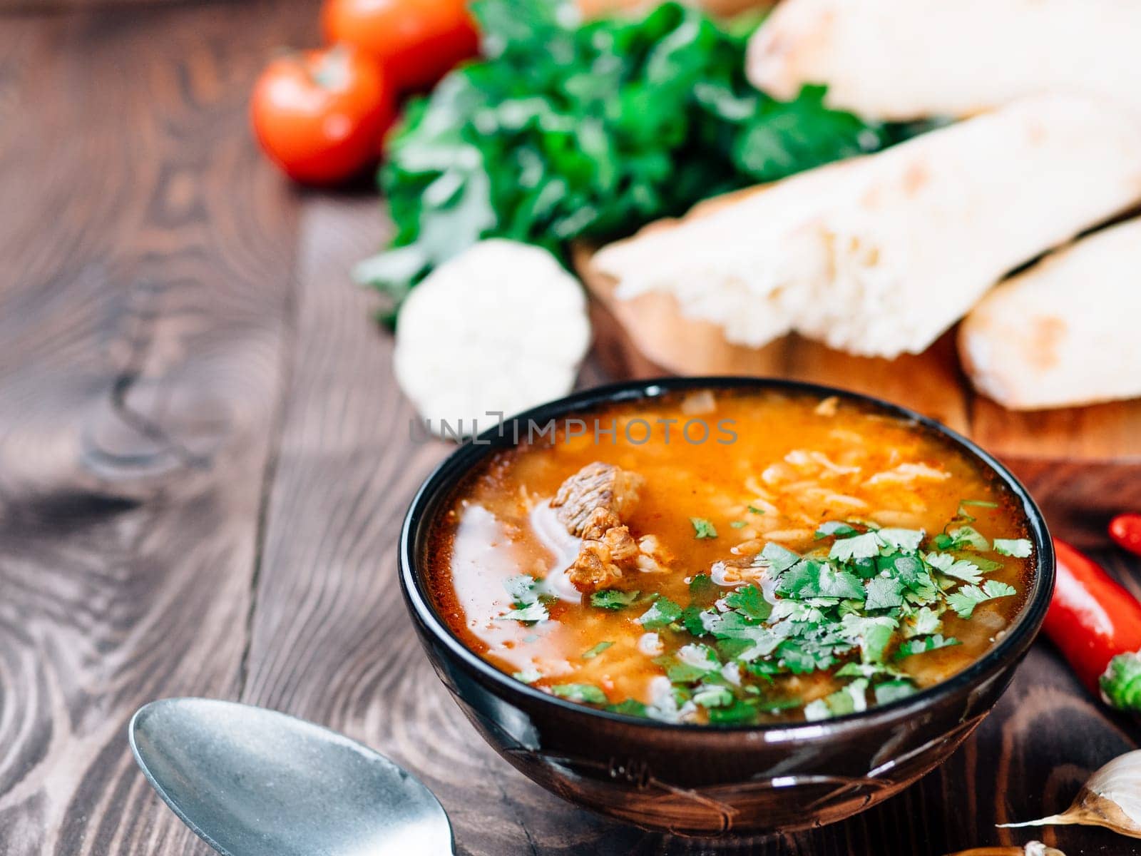 Traditional Georgian kitchen-soup Kharcho with meat, rice and fresh cilantro. Spicy soup Kharcho on wooden table with traditional bread Shotis Puri and vegetables. Selective focus. Copy space for text
