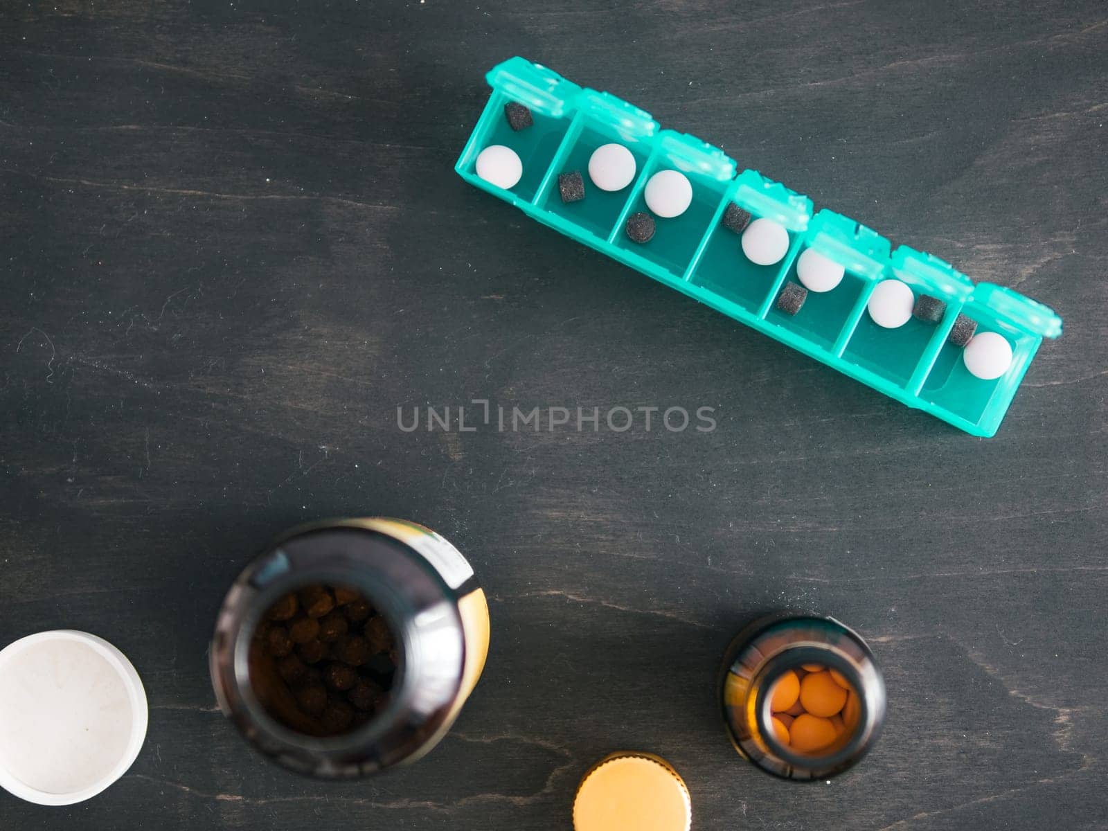 Top view of seven day pill box with pills. Green pill-box with pills visible. Open pill box and jars on dark wooden table. Copy space. Top view or flat lay.Healthy lifestyle and medical concept