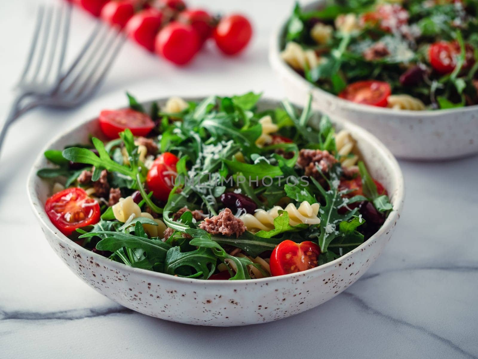 Warm salad with tuna, arugula, tomatoes, red bean, pasta. Idea and recipe for healthy lunch or dinner. Two bowls with warm salads on marble tabletop. Ideas and recipes for healthy dinner or lunch