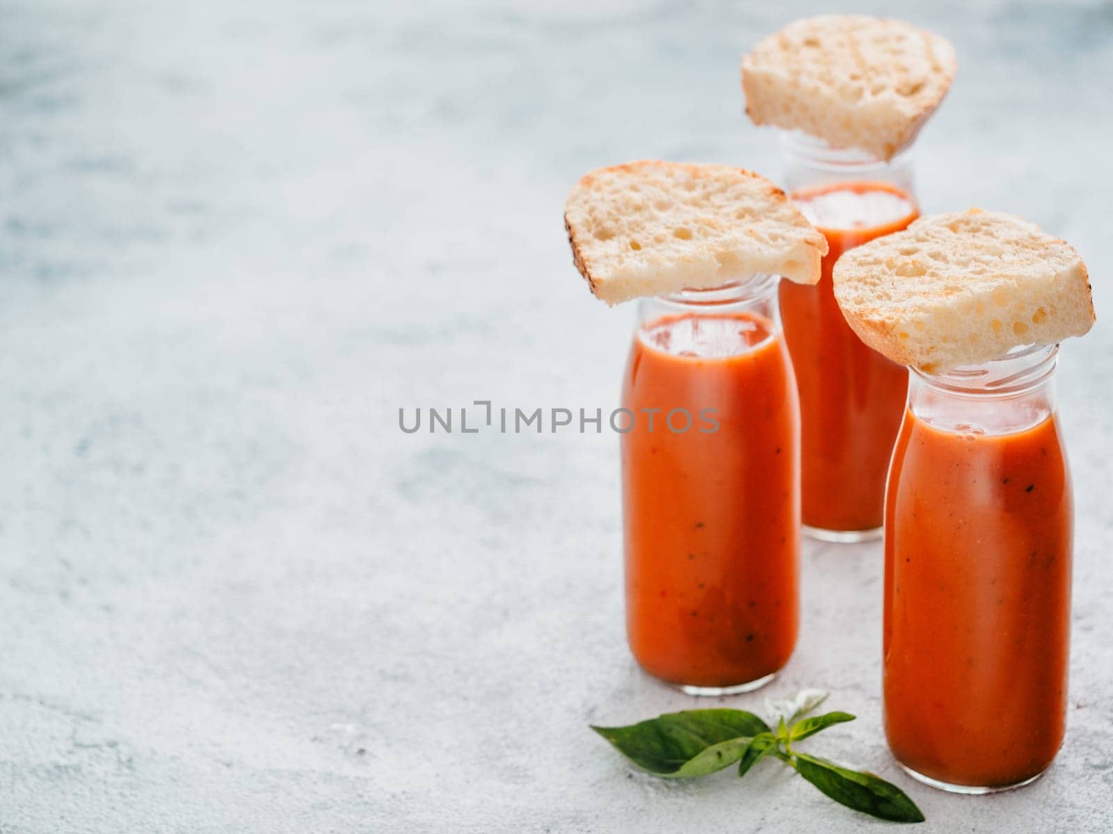 Delicious gaspacho soup in glass bottles. Traditional spanish cold soup puree gaspacho or gazpacho on gray cement background with copy space for text