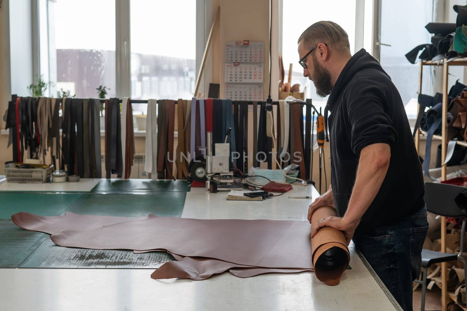 Leatherworker unrolls rolls of leather in workshop. by mrwed54
