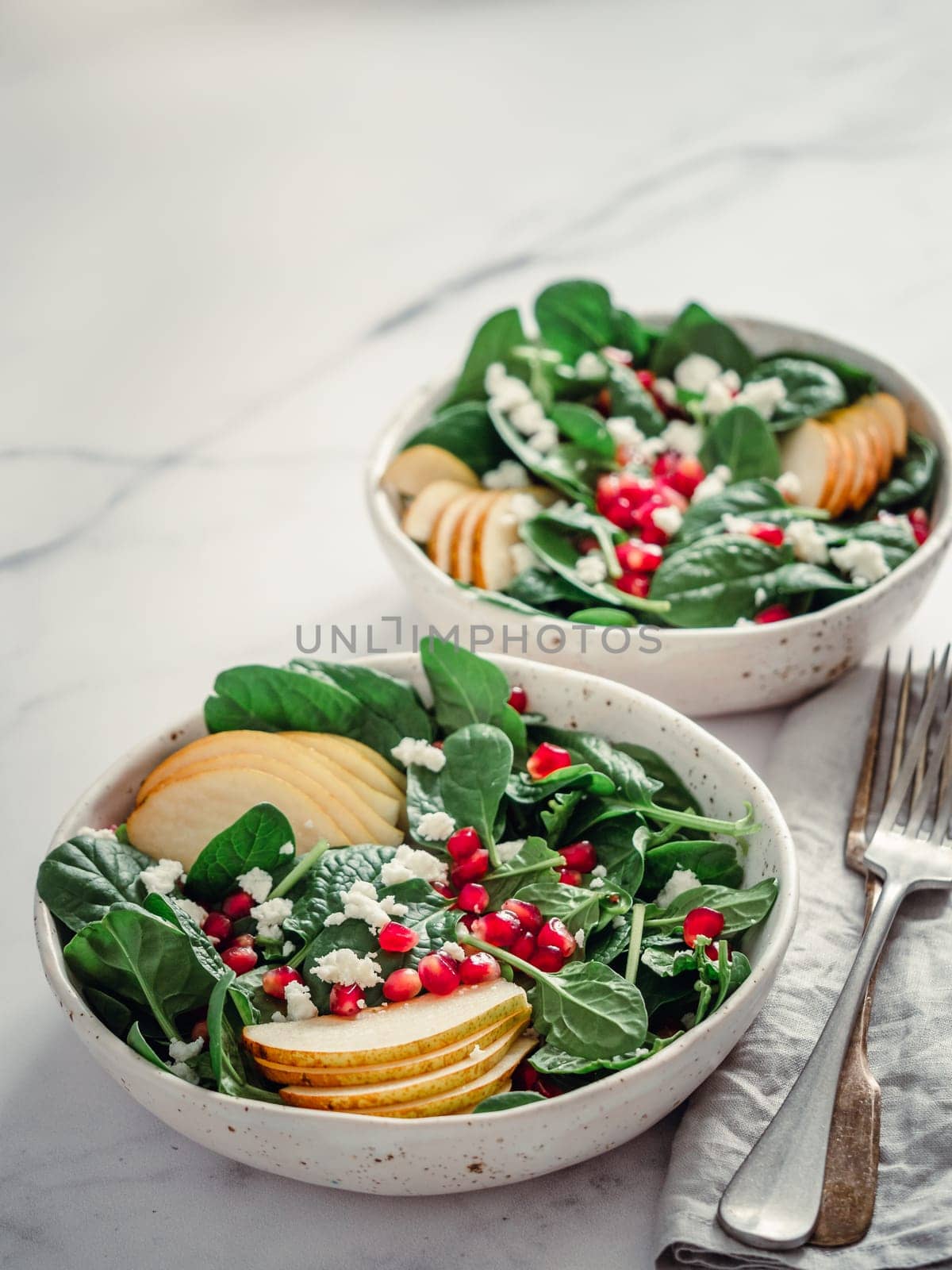 Vegan salad bowl with spinach, pear, pomegranate, cheese on marble tabletop. Vegan breakfast, vegetarian food, diet concept. Vertical. Copy space for text.