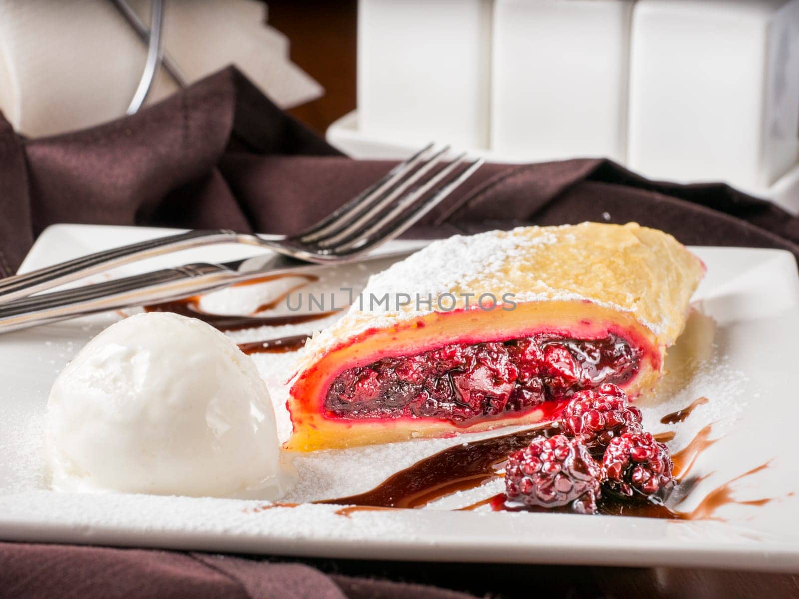 Sweet dessert - strudel with cherry and blackberry on white plate with ice cream at restaurant table