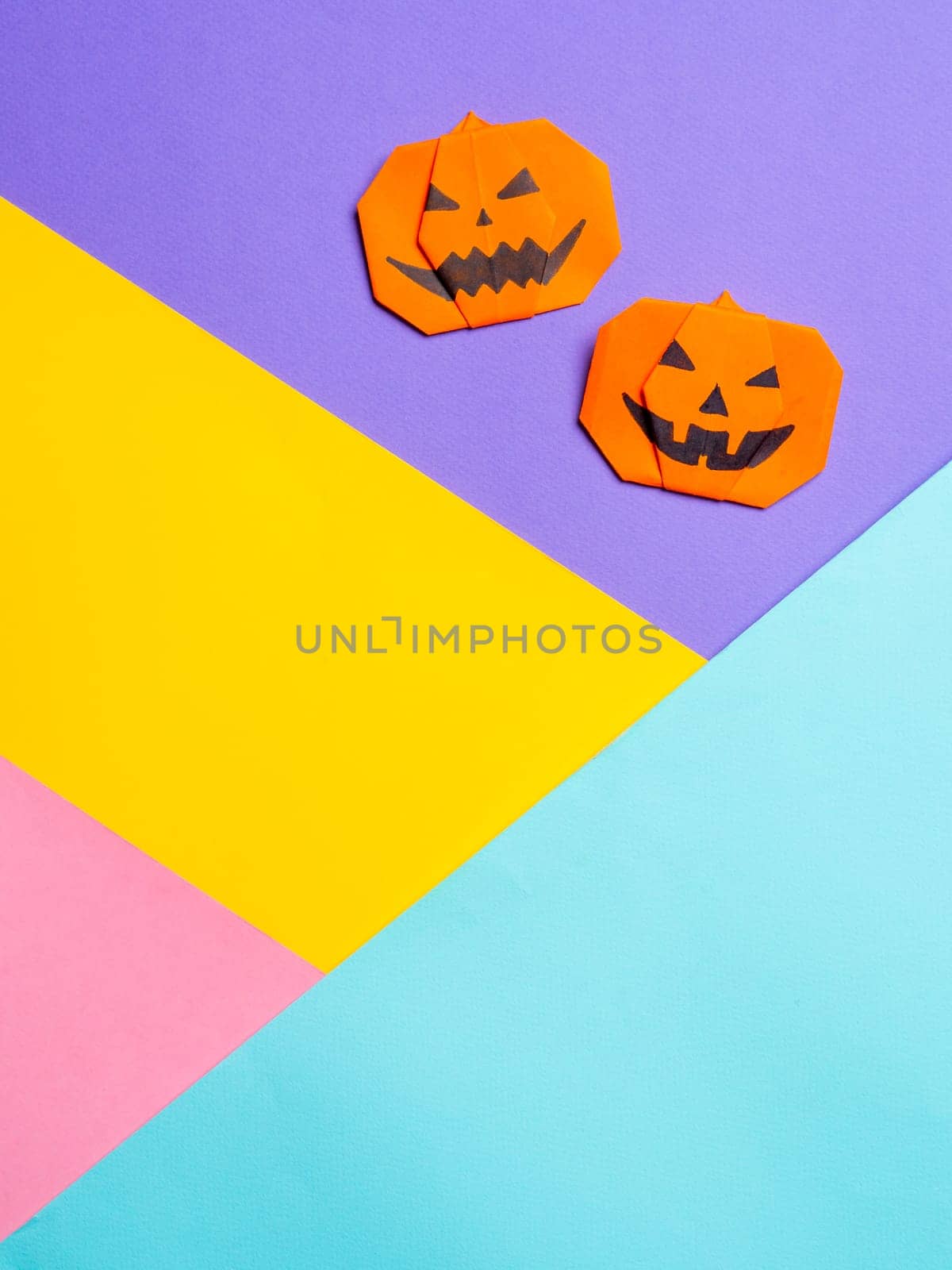 Halloween concept. Paper origami pumpkin on colorful background. Simple idea for halloween - easy made paper pumpkins on multicolor blue, yellow, pink, lilac background. Copy space for text. Vertical