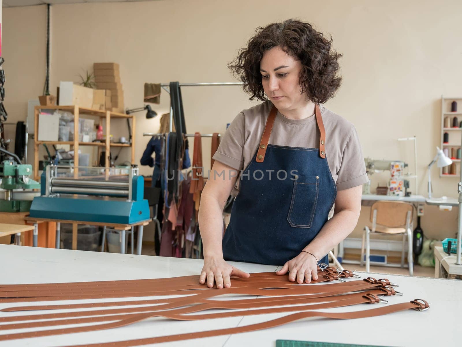 Caucasian woman makes belts from genuine leather in a workshop. by mrwed54
