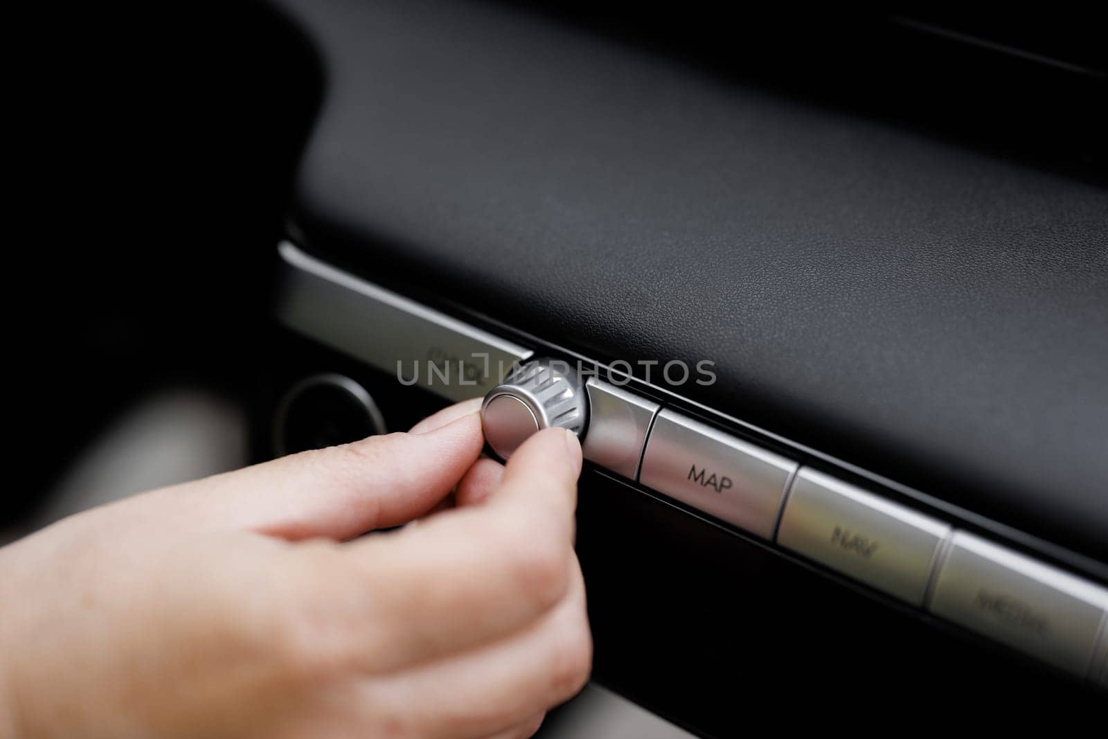 Car dashboard volume knob. Driver's hand adjusts volume control of car radio. Female hand control radio or music in car in motion. Turns up the volume of the music in the car