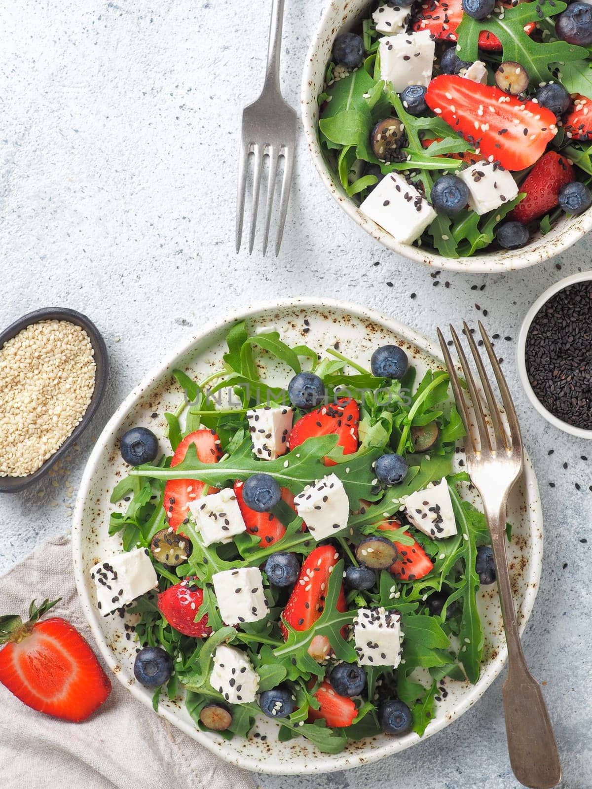 Salad with arugula,feta cheese and berries-strawberry,blueberry,in craft plate on gray cement background.Summer salad idea and recipe for healthy vegetarian lunch,dinner.Top view.Copy space. Vertical