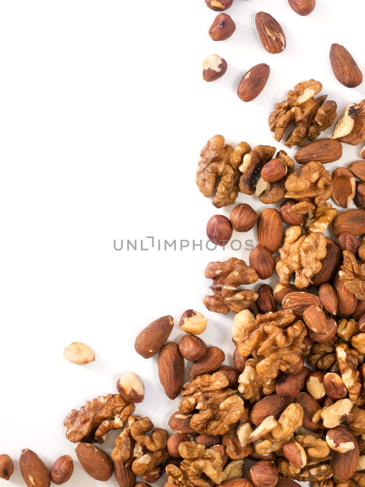 Background of mixed nuts - hazelnuts, walnuts, almonds - with copy space. Isolated one edge. Top view or flat lay. Vertical image