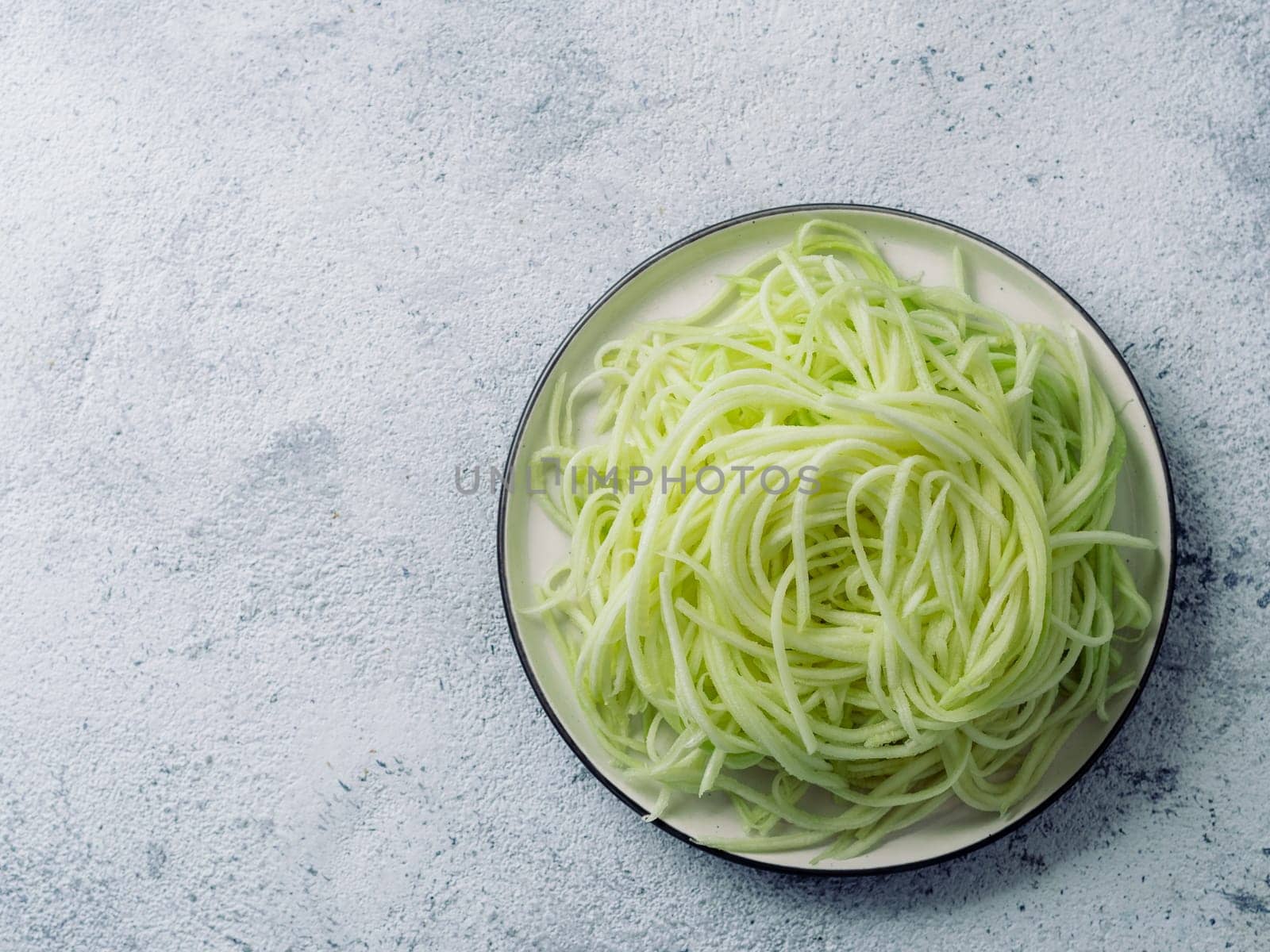 Zucchini noodles on plate. Vegetable noodles - green zoodles or courgette spaghetti on plate over gray background. Clean eating, raw vegetarian food concept. Copy space for text. Top view or flat lay