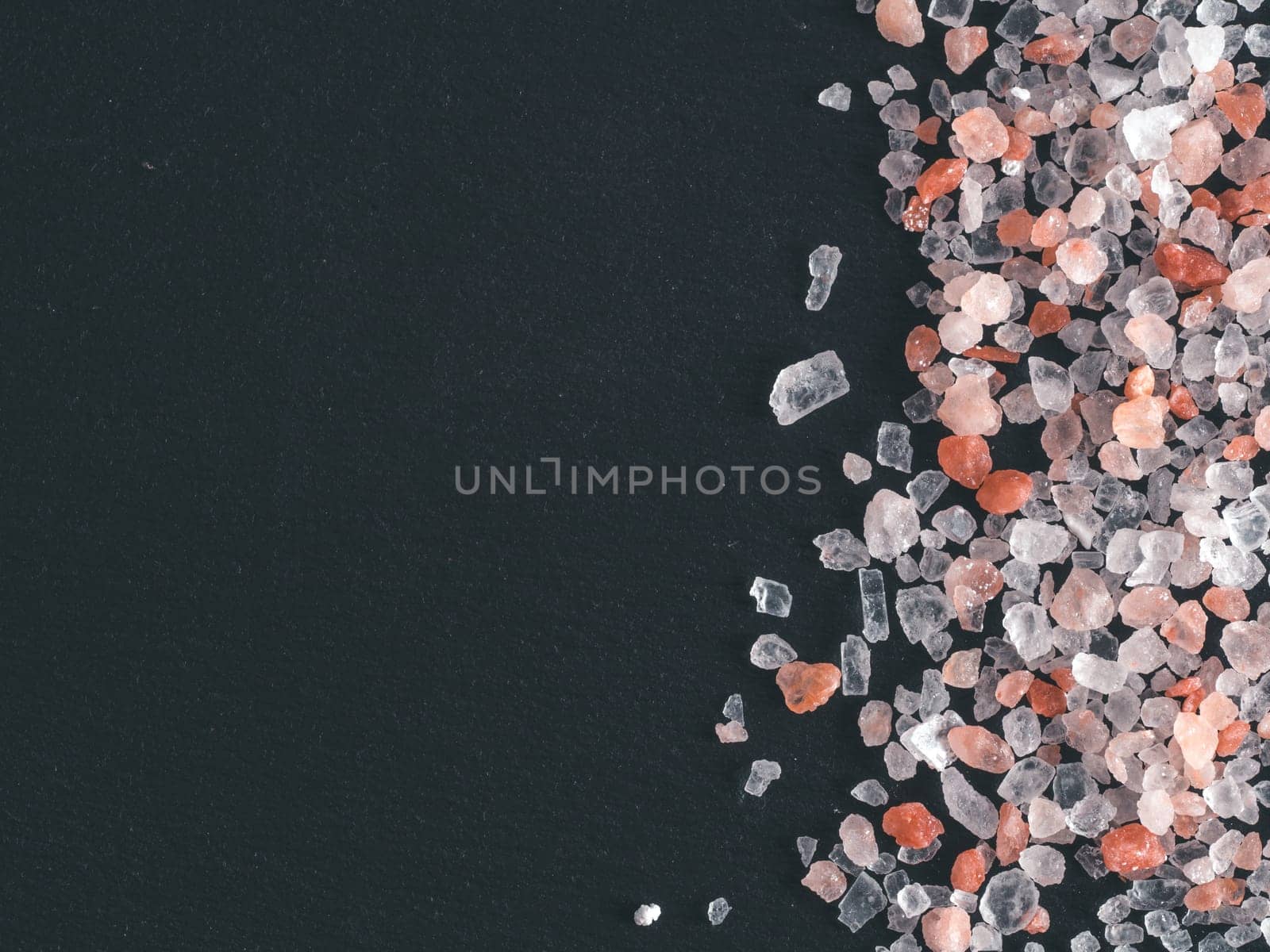 Himalayan pink salt in crystals on black stone background. Copy space