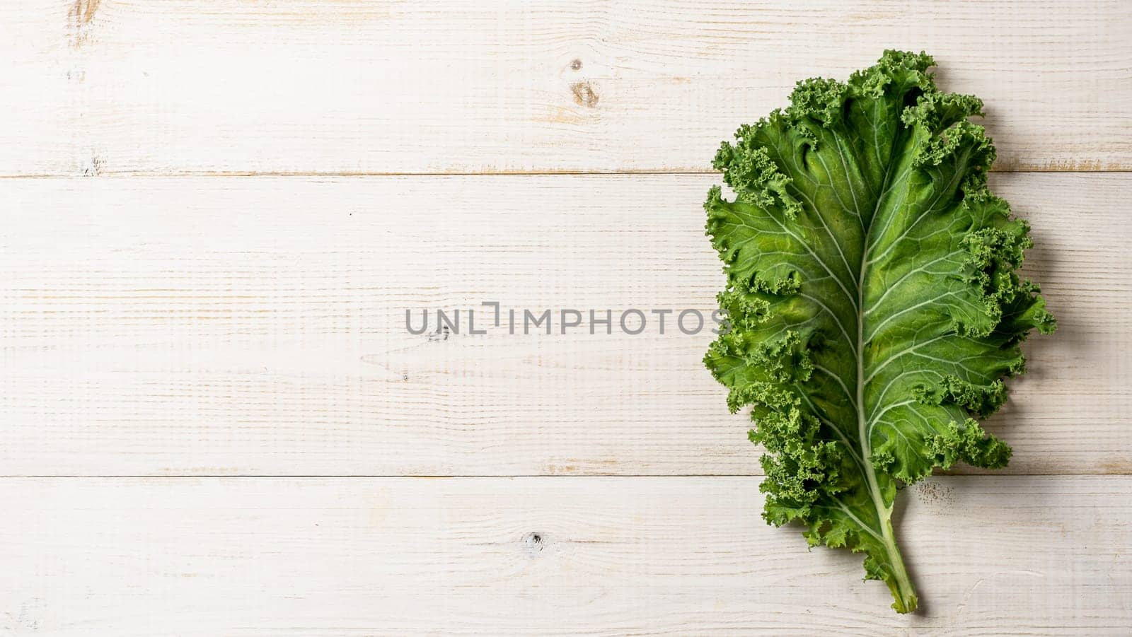 Green kale leaf on white wood table, copy space, top view by fascinadora