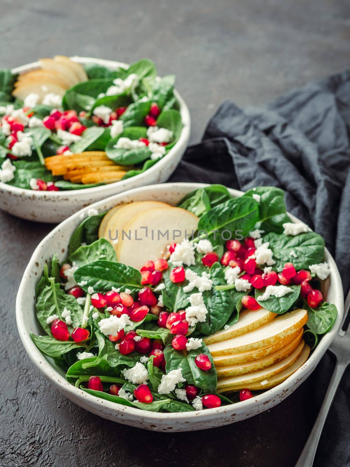 Vegan salad bowl with spinach, pear, pomegranate, cheese on black background. Vegan breakfast, vegetarian food, diet concept. Vertical. Top view or flat lay. Copy space for text.
