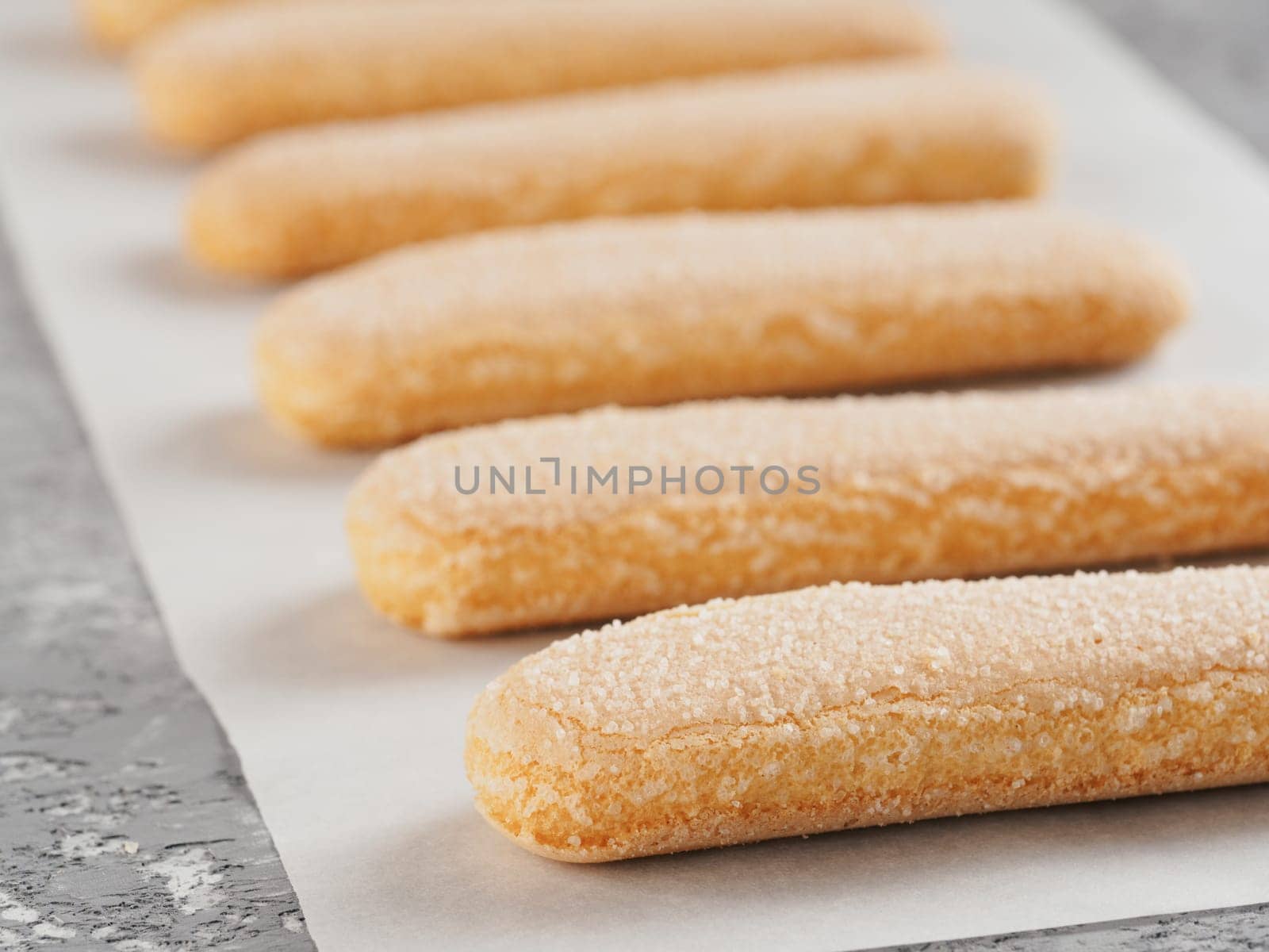 Close up view of ladyfinger biscuit cookie on gray concrete background. Italian cookie savoiardi in row on baking paper.