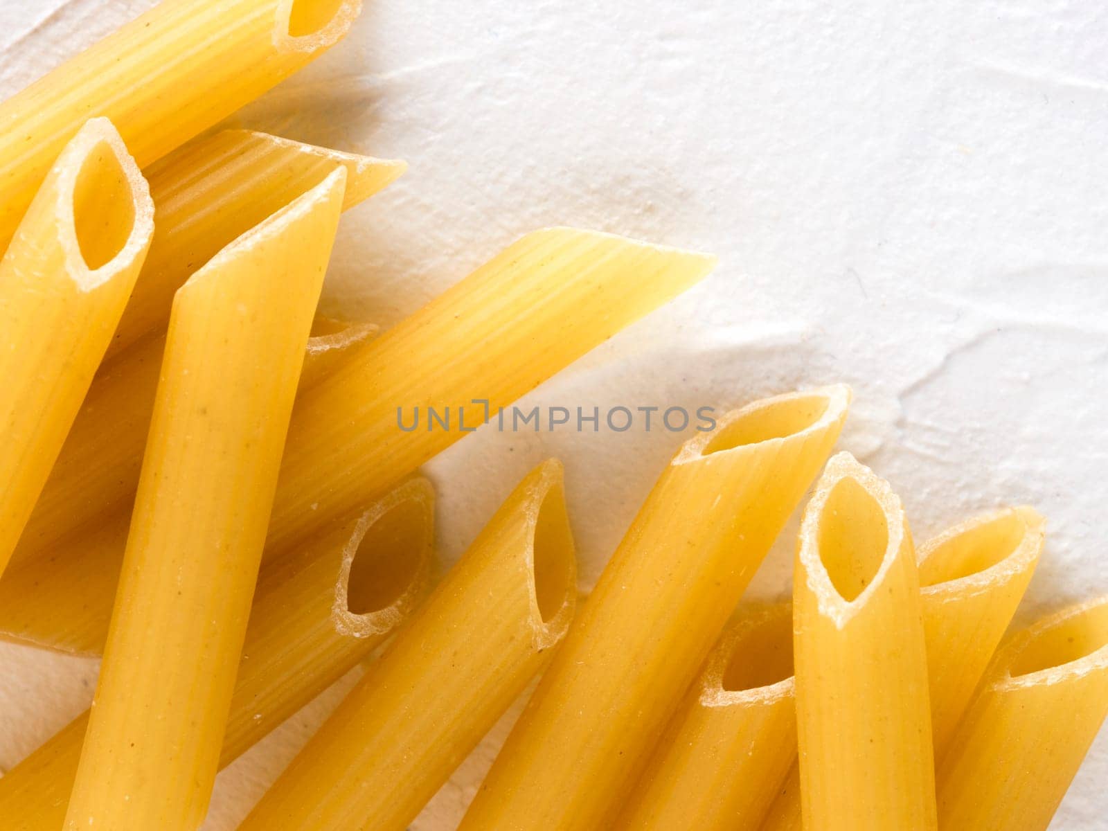 raw pasta penne on white background by fascinadora