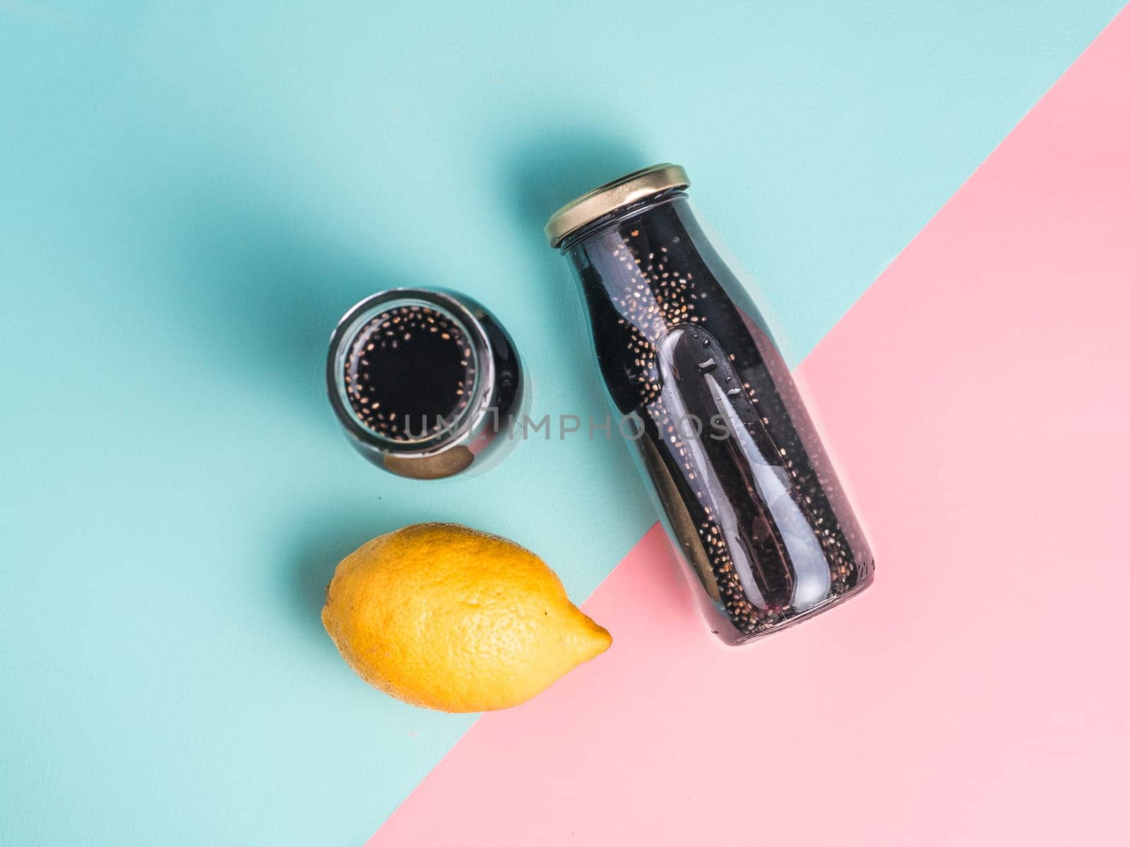 Detox activated charcoal black chia water or lemonade with lemon on colorful blue and pink background.Two bottle with black chia infused water.Detox drink idea and recipe.Vegan food and drink.Top view
