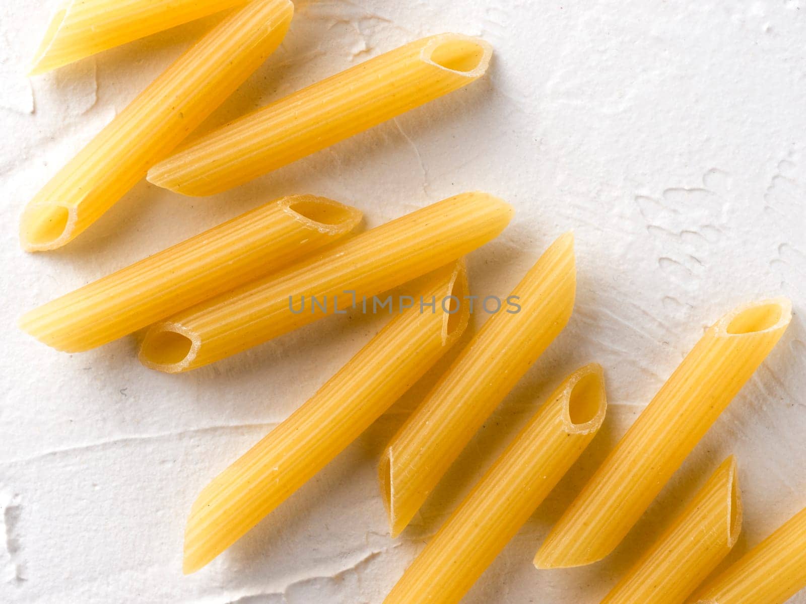 raw pasta penne on white background by fascinadora