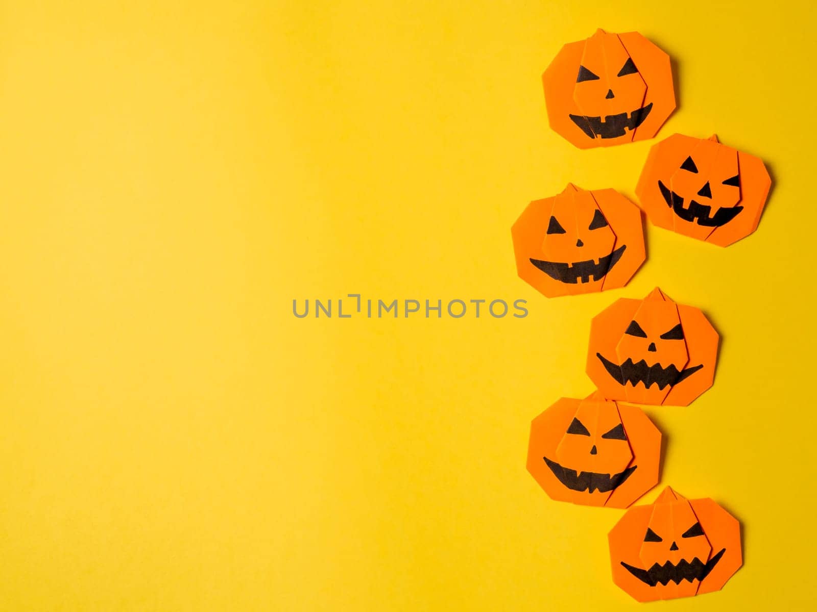 Halloween concept. Paper origami pumpkin on yellow background. Simple idea for halloween - easy made paper pumpkins on trendy color Ceylon Yellow background. Copy space for text.