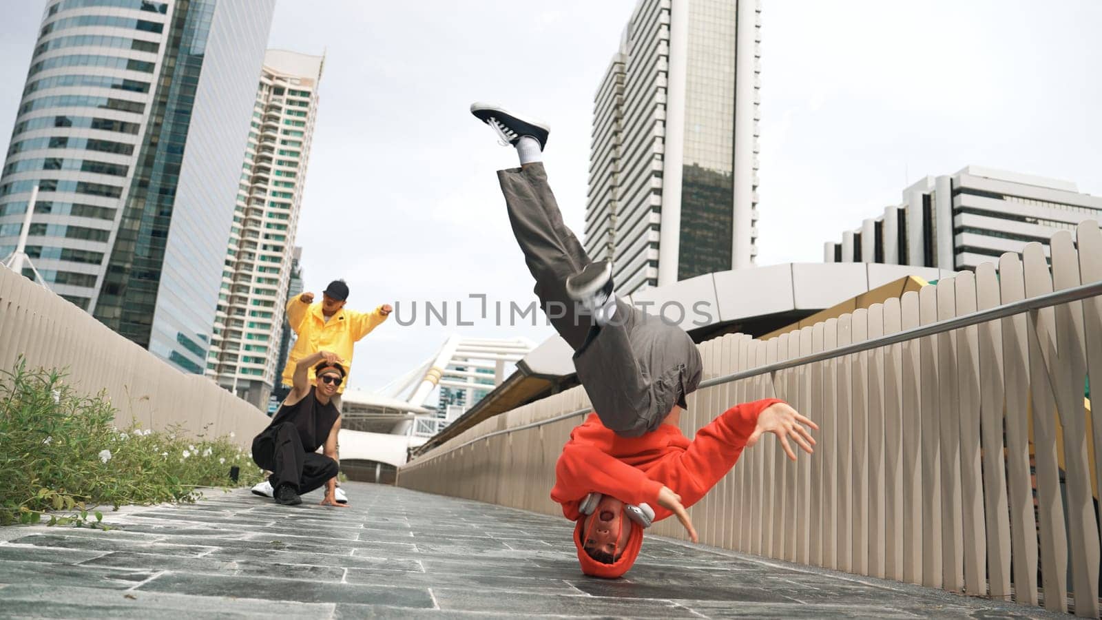 Young happy hipster perform break dancing or foot step with friend moving to hiphop music together. Skilled dancer doing freeze pose and waving hand. Modern lifestyle. Outdoor music 2024. Sprightly.