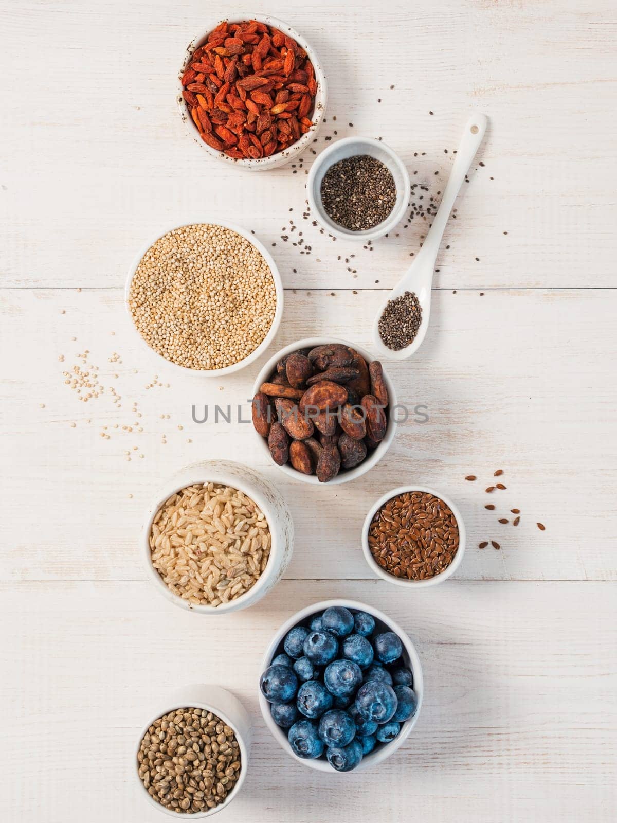 Various superfoods in small bowl on white wooden table.Selection super food.Superfood as blueberry, chia, raw cocoa bean, goji, hemp seeds, quinoa, brown rice. Copy space.Top view or flat lay.Vertical