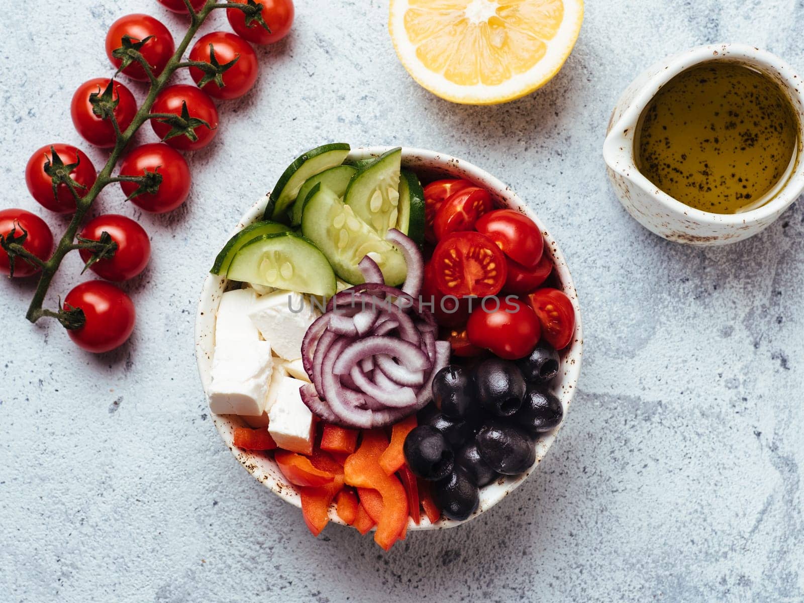 Greek Salad Bowl on gray cement background. Above view of Bowl Greek Salad with olive oil and ingredients. Trendy food. Idea, recept and concept of modern healthy food. Copy space for text.