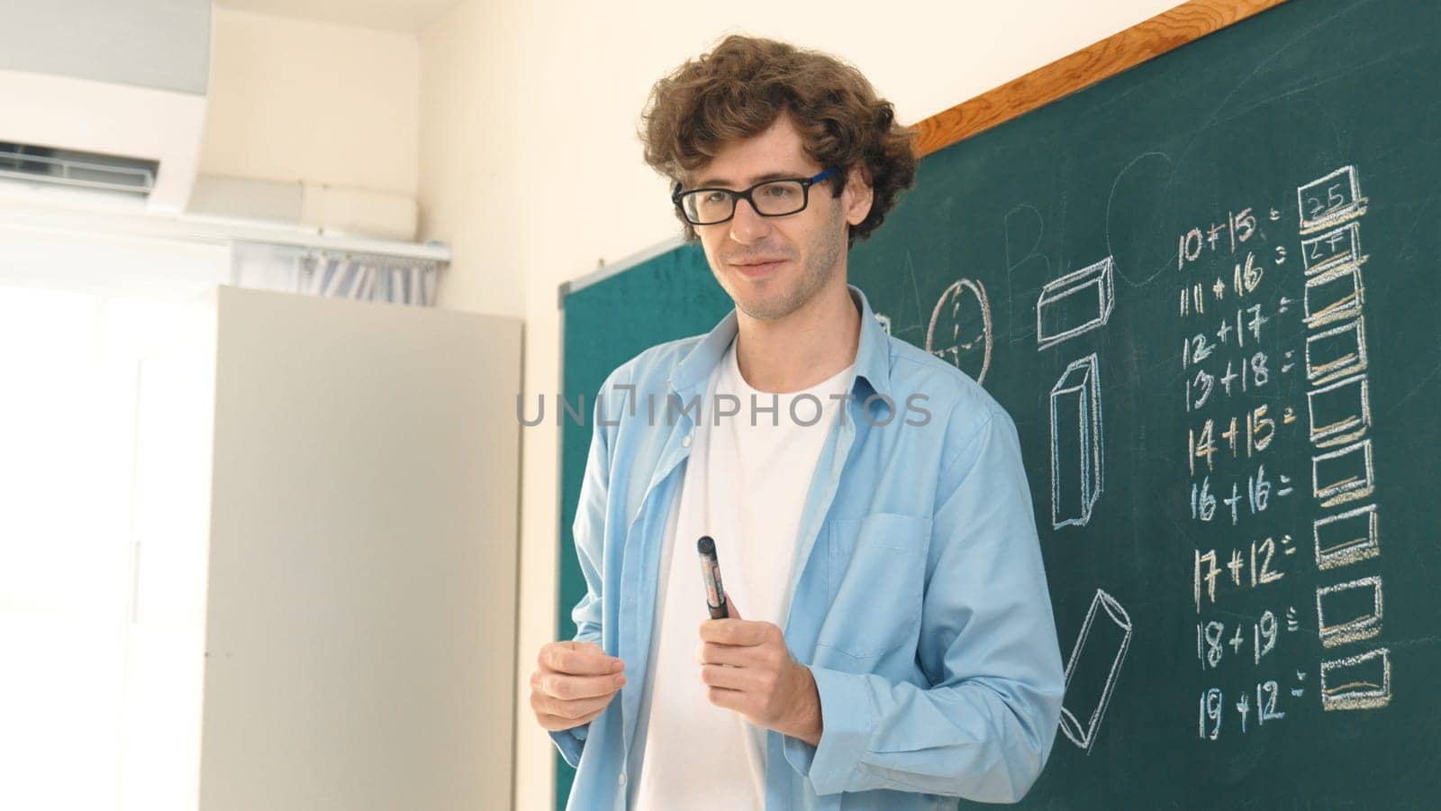Caucasian teacher looking at student while standing at blackboard. Low angle camera of professional instructor teaching and explain math theory while answer question from diverse student. Pedagogy.