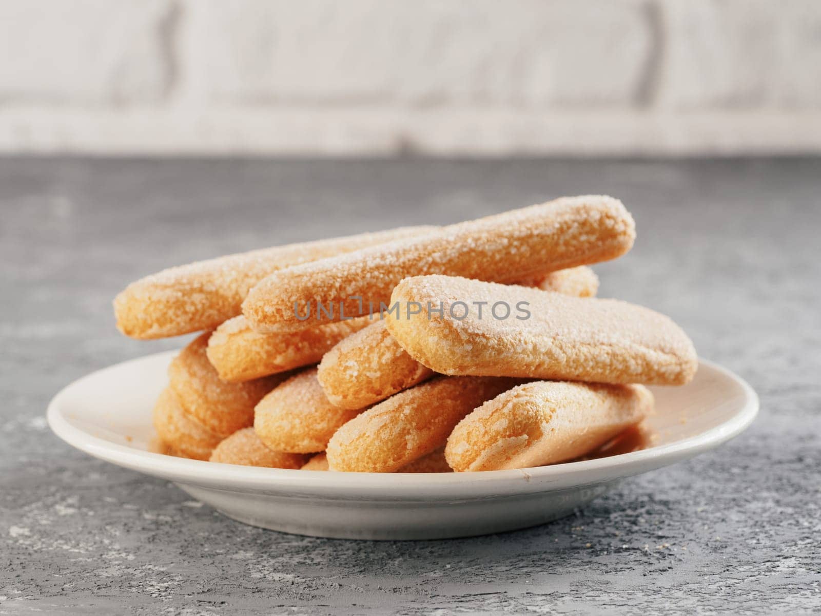 Close up view of ladyfinger biscuit cookie in plate on gray concrete background. Italian cookie savoiardi. Copy space.