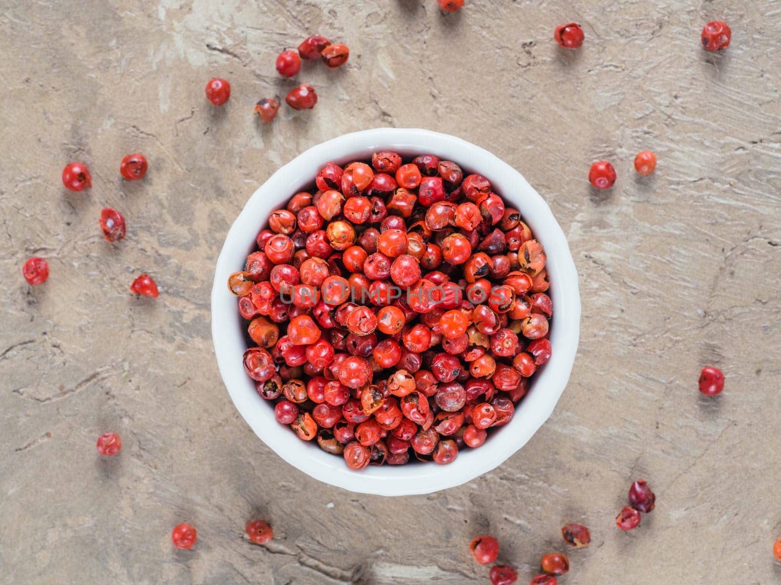 Pile with dried pink pepper berries on brown concrete background. Close up view of pink peppercorn. Top view or flat-lay.