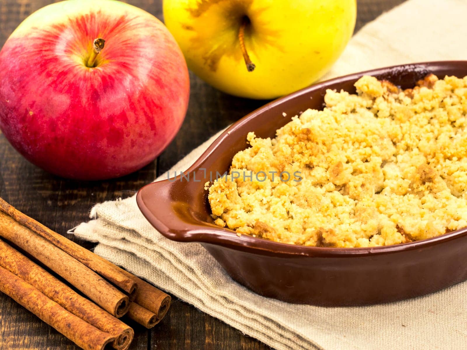 Homemade apple cramble cake with fresh apples and cinnamon sticks on rustic dark wooden background