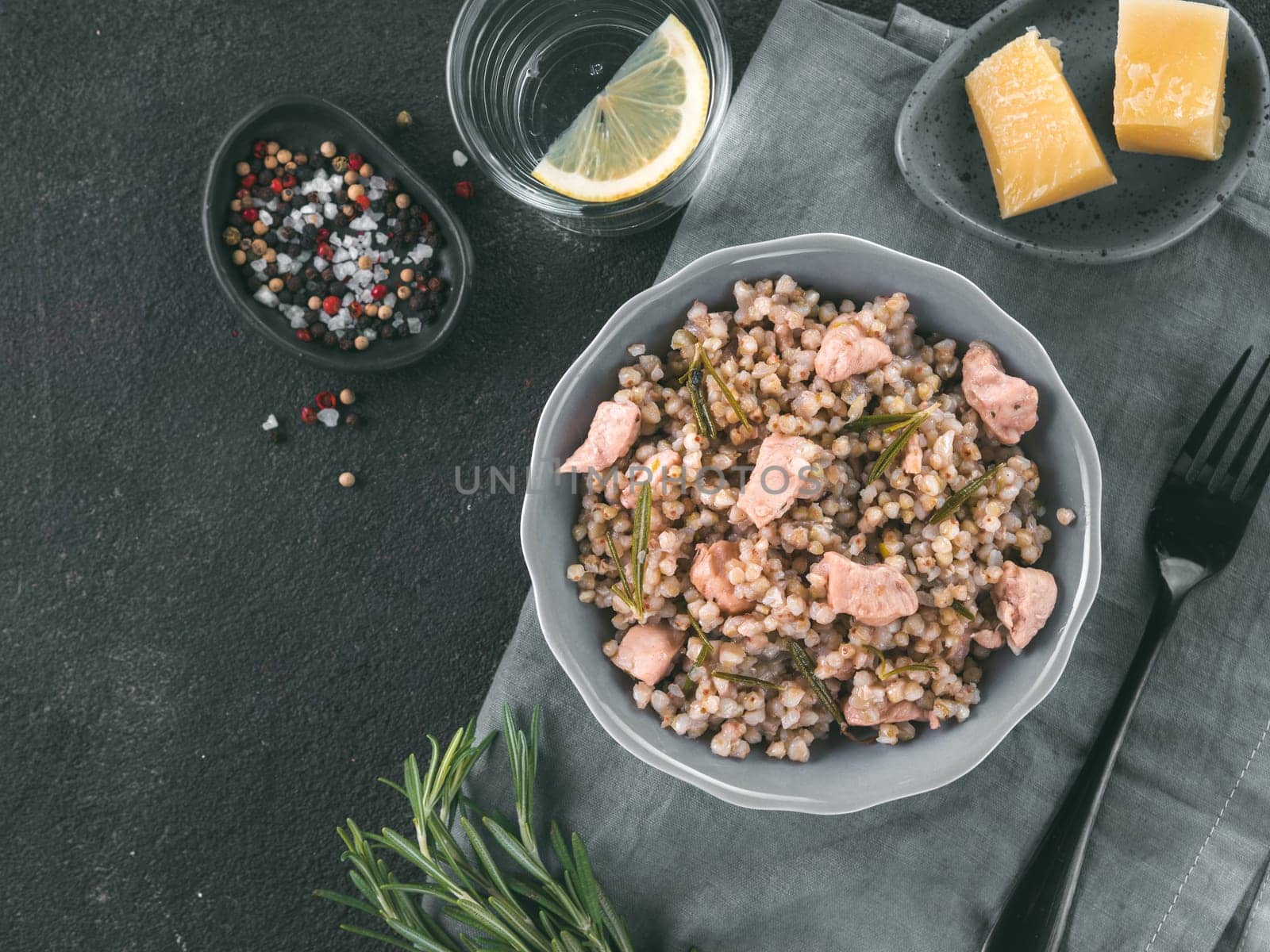 Raw buckwheat risotto with chicken meat and rosemary served parmesan cheese in gray plate on black cement background. Gluten-free and buckwheat recipe ideas. Copy space. Top view or flat-lay.