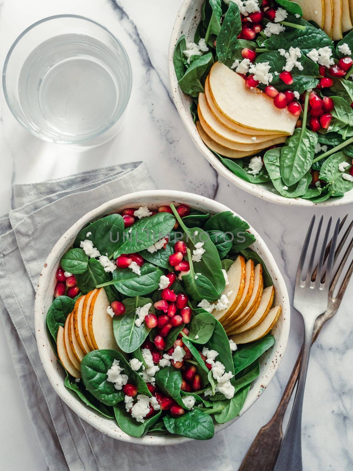 Vegan salad bowl with spinach, pear, pomegranate, coconut cramble or cottage cheese on marble tabletop. Vegan breakfast, vegetarian food, diet concept. Vertical. Top view or flat lay.