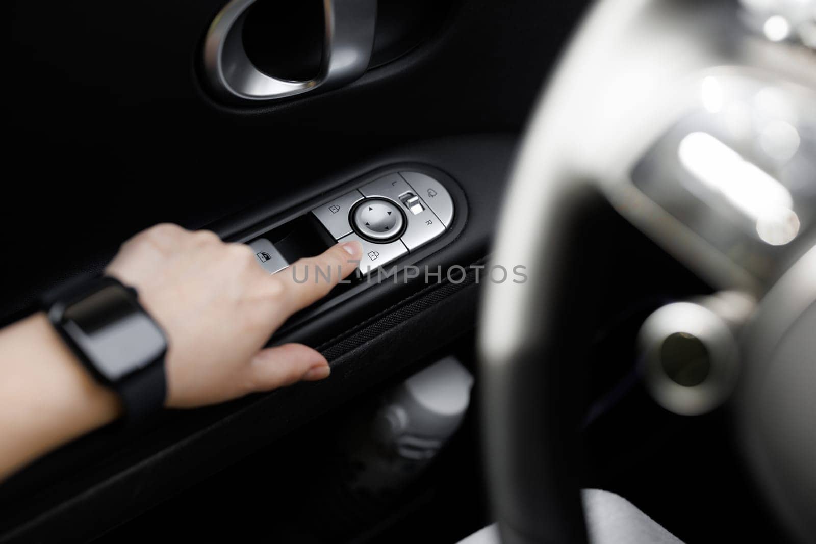 The buttons for closing the car doors are pressed by hand on the armrest. Close-up view of car interior. Window and mirror control panel on driver's door, detail of modern electric car by uflypro