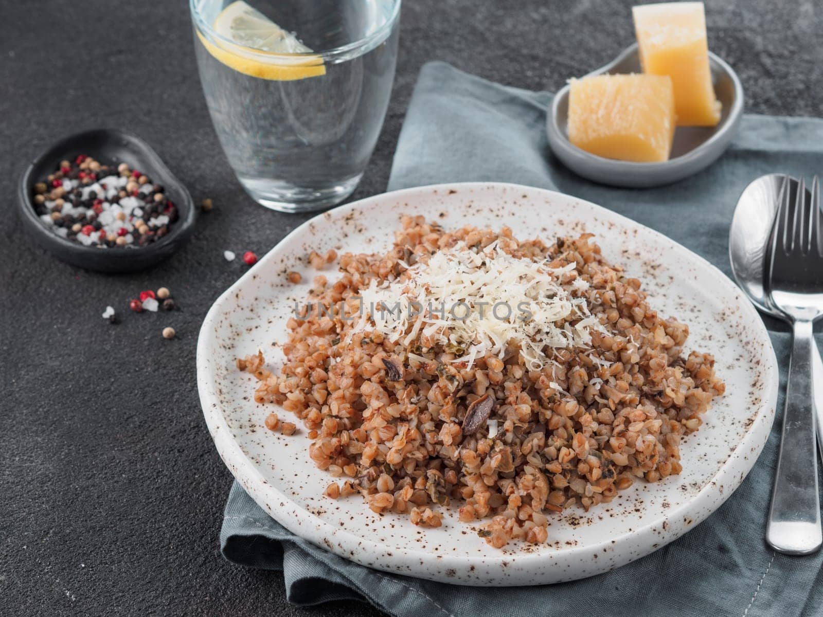 Buckwheat risotto with dried mushrooms in craft plate on black cement background. Gluten-free and vegetarian buckwheat recipe ideas. Copy space