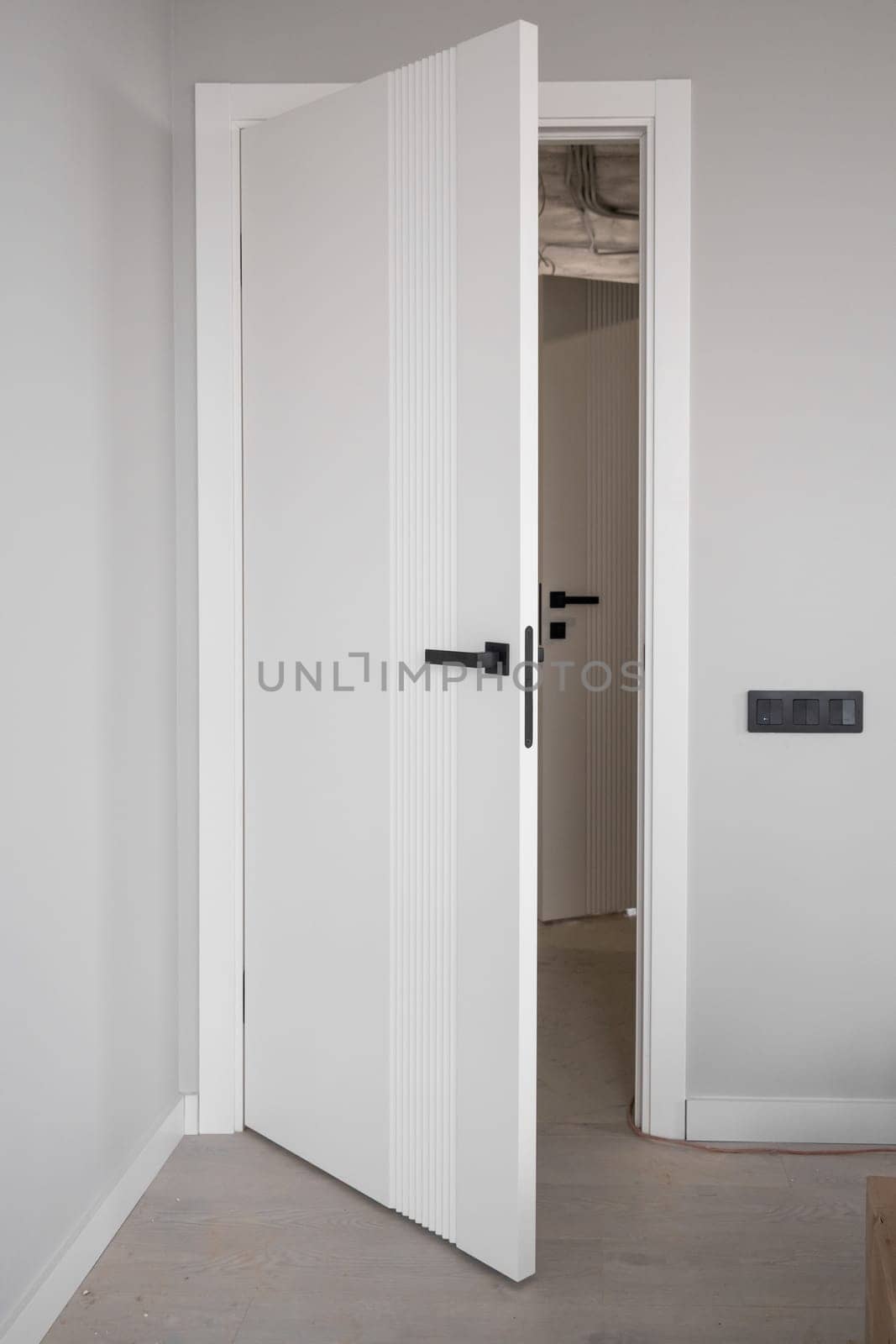 An open white door with a manual one in a renovated apartment. Moving to a new apartment. Doorknob on an open door with a ladder in the room during renovation and painting work.