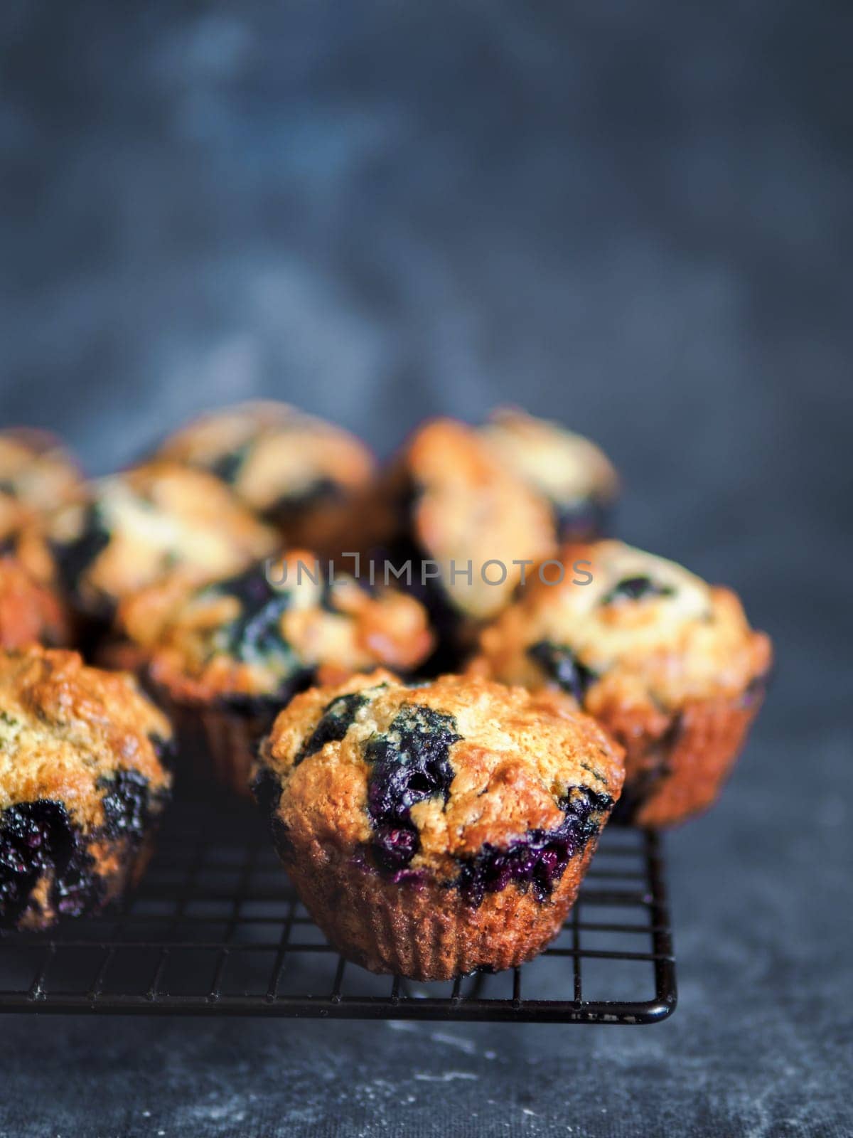 Homemade vegan blueberry muffins on cooling rack. Vegetarian egg-free muffins on dark background. Vertical. Copy space for text or design.