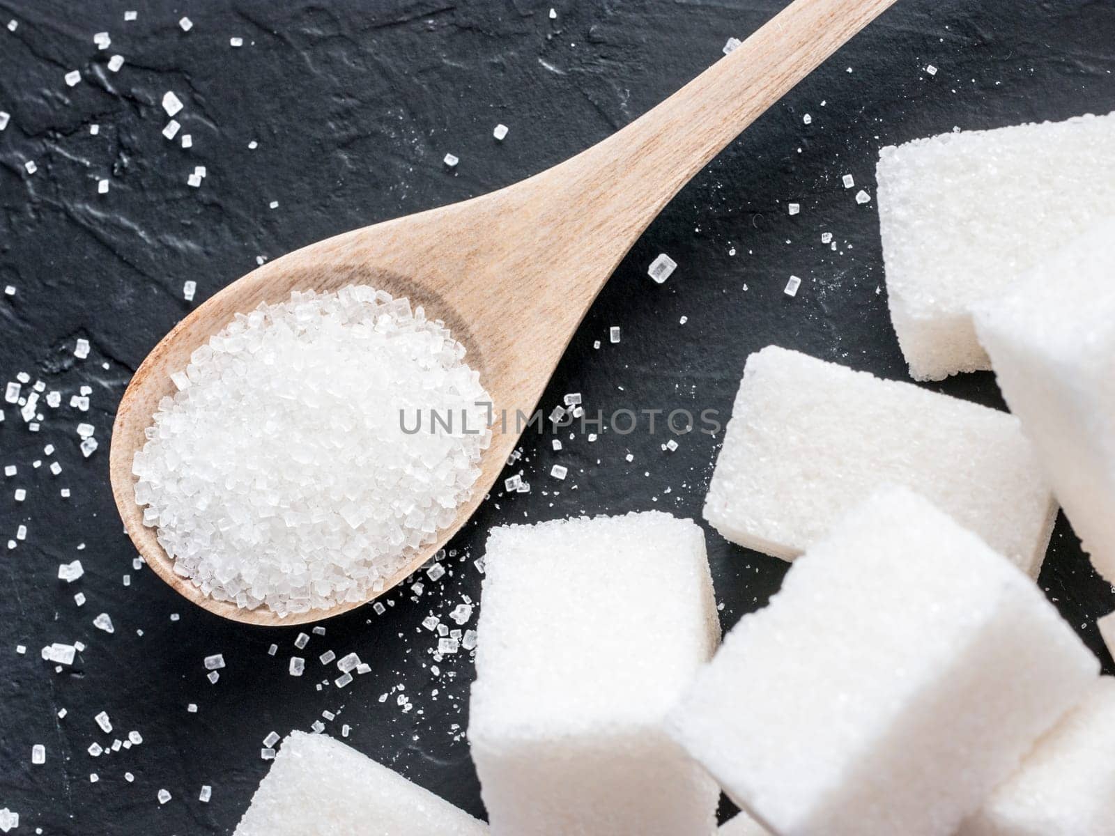 background of sugar cubes and sugar in spoon. White sugar on black background. Sugar cubes and granulated in wooden spoon