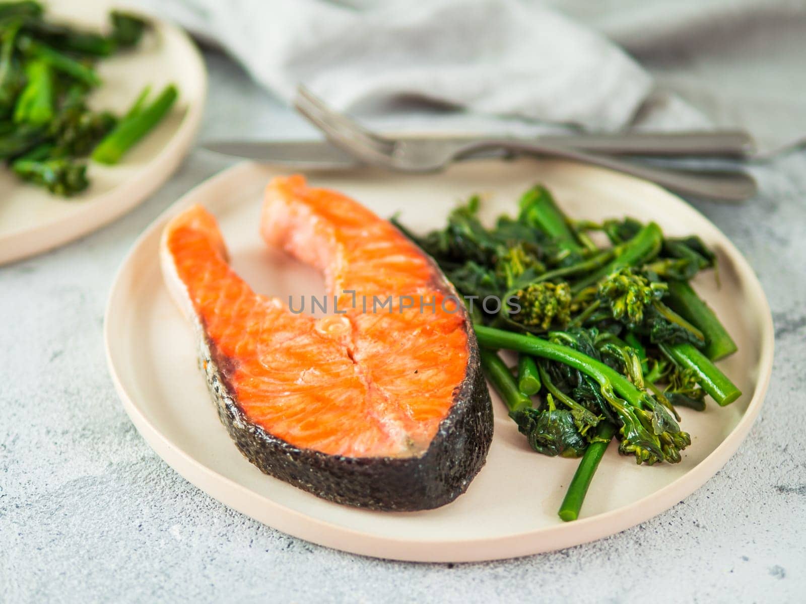 Ready-to-eat grilled salmon steak and greens - baby broccoli or broccolini and spinach on rustic craft plate over gray background. Keto diet dish.