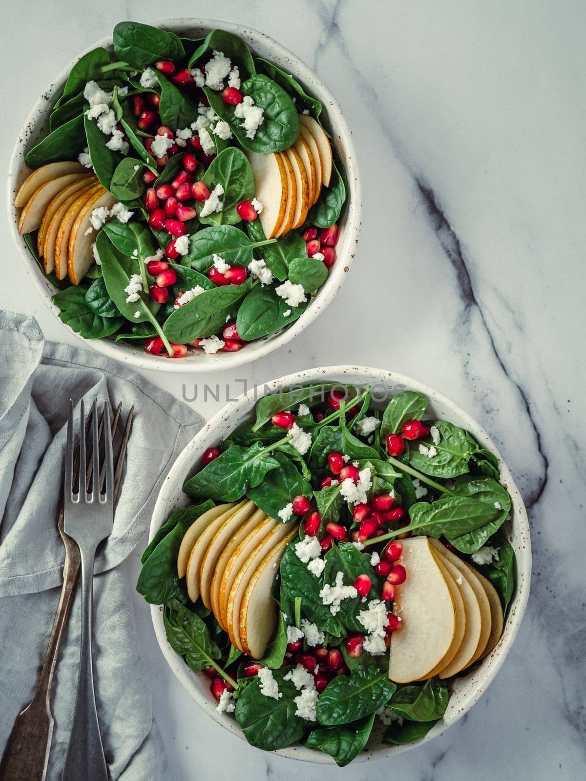 Vegan salad bowl with spinach, pear, pomegranate, cheese on marble tabletop. Vegan breakfast, vegetarian food, diet concept. Vertical. Top view or flat lay.