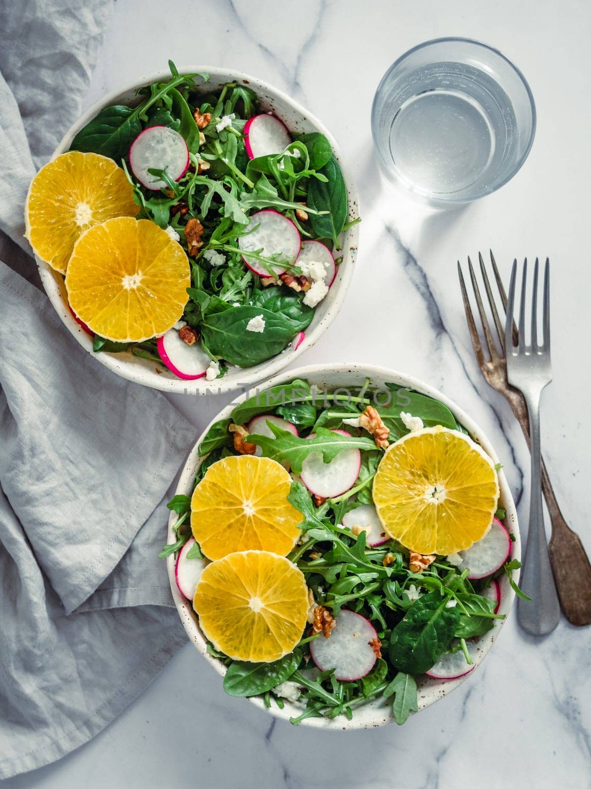 Vegan salad bowl with oranges, spinach, arugula, radish, nut. Top view. Vegan breakfast, vegetarian food, diet concept. Two bowls with salad on white marble tabletop. Vertical