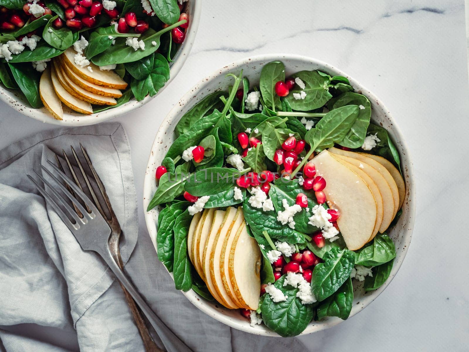 Fresh salad with baby spinach, pear, pomegranate and cottage cheese. Two bowls with delicious summer fruit salad on marble table. Copy space for text. Ideas and recipes for healthy breakfast or lunch