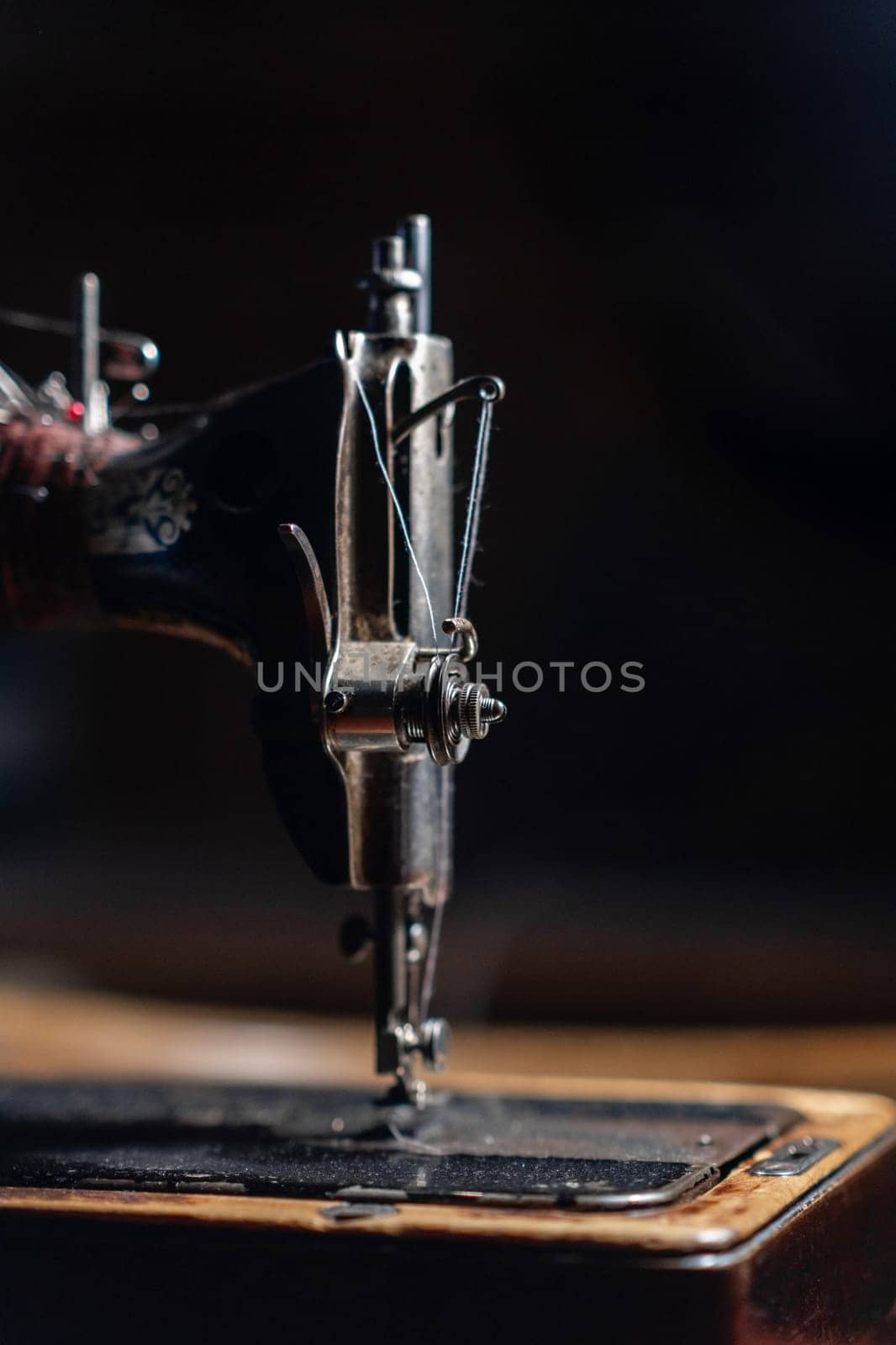 An old sewing machine stands on the table at home ready to work and sew. Classic retro style manual sewing machine ready for sewing work. The machine is old style made of metal with floral patterns