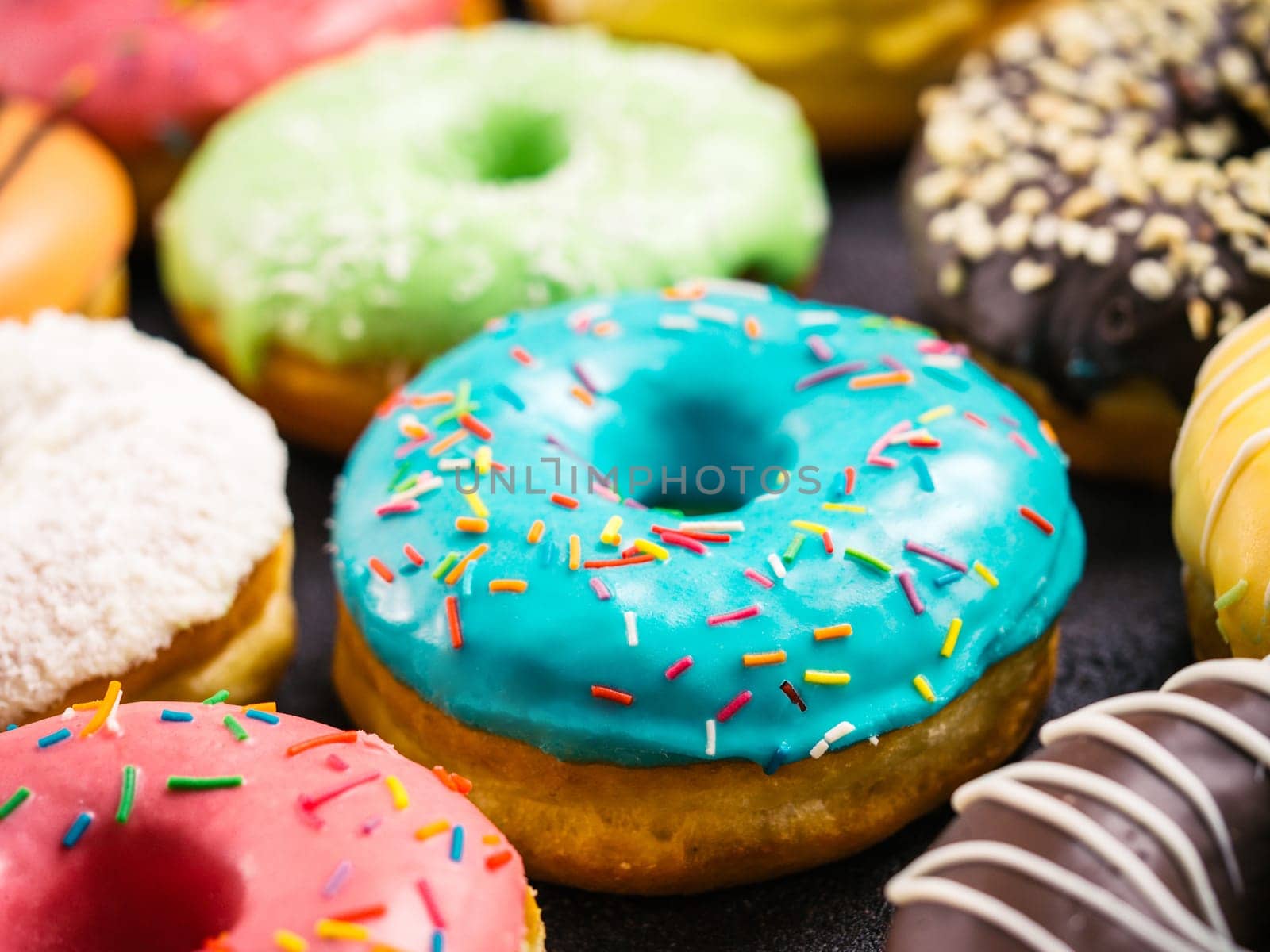 Close up view of assorted colorful donuts on dark background. Focus on blue glazed doughnut with sprinkles. Shallow DOF,