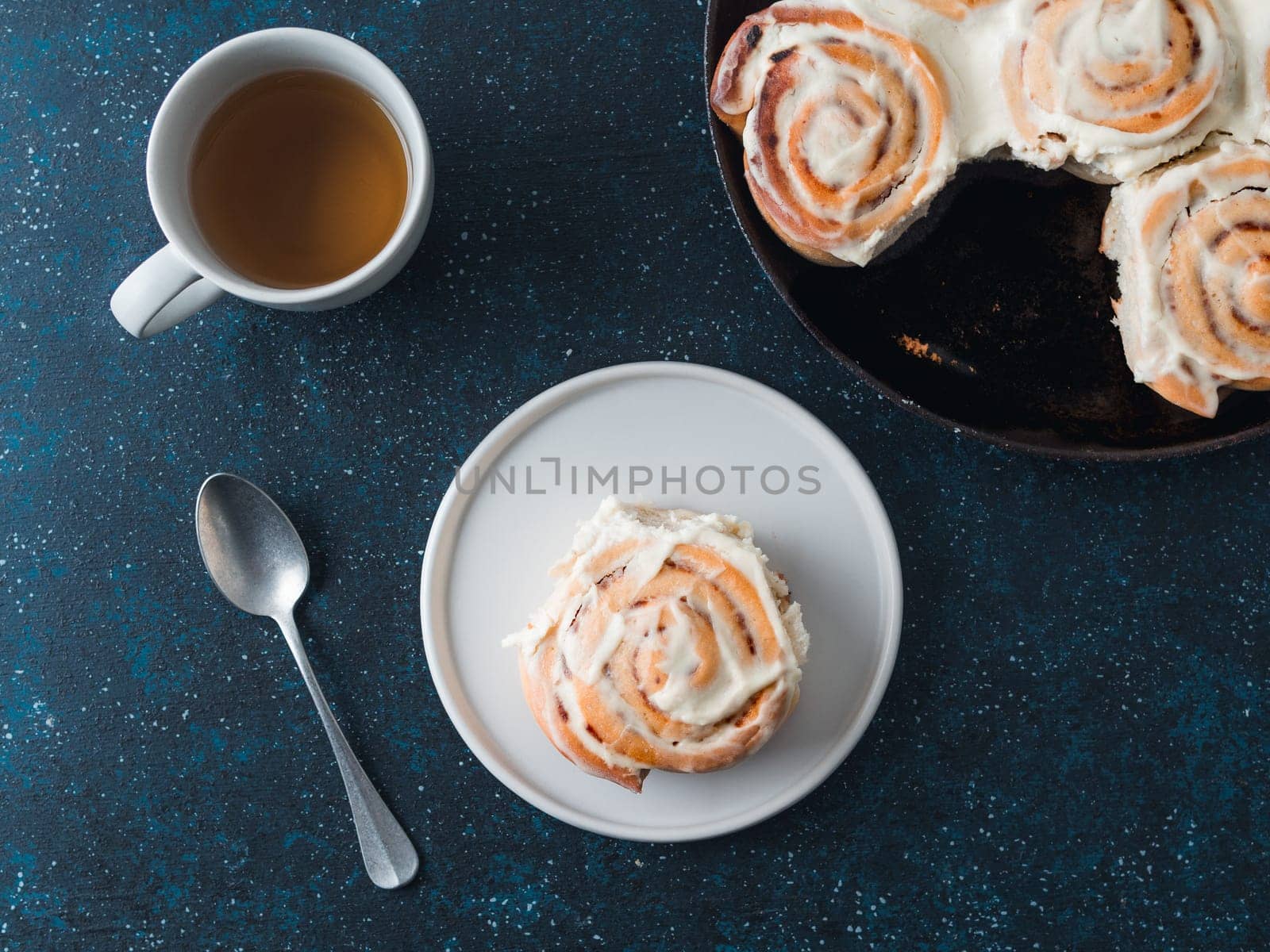 Idea and recipe pastries - perfect cinnamon rolls with topping.Vegan swedish cinnamon buns Kanelbullar with pumpkin spice,topping vegan cream cheese in plate with tea cup on table.Flat lay or top view