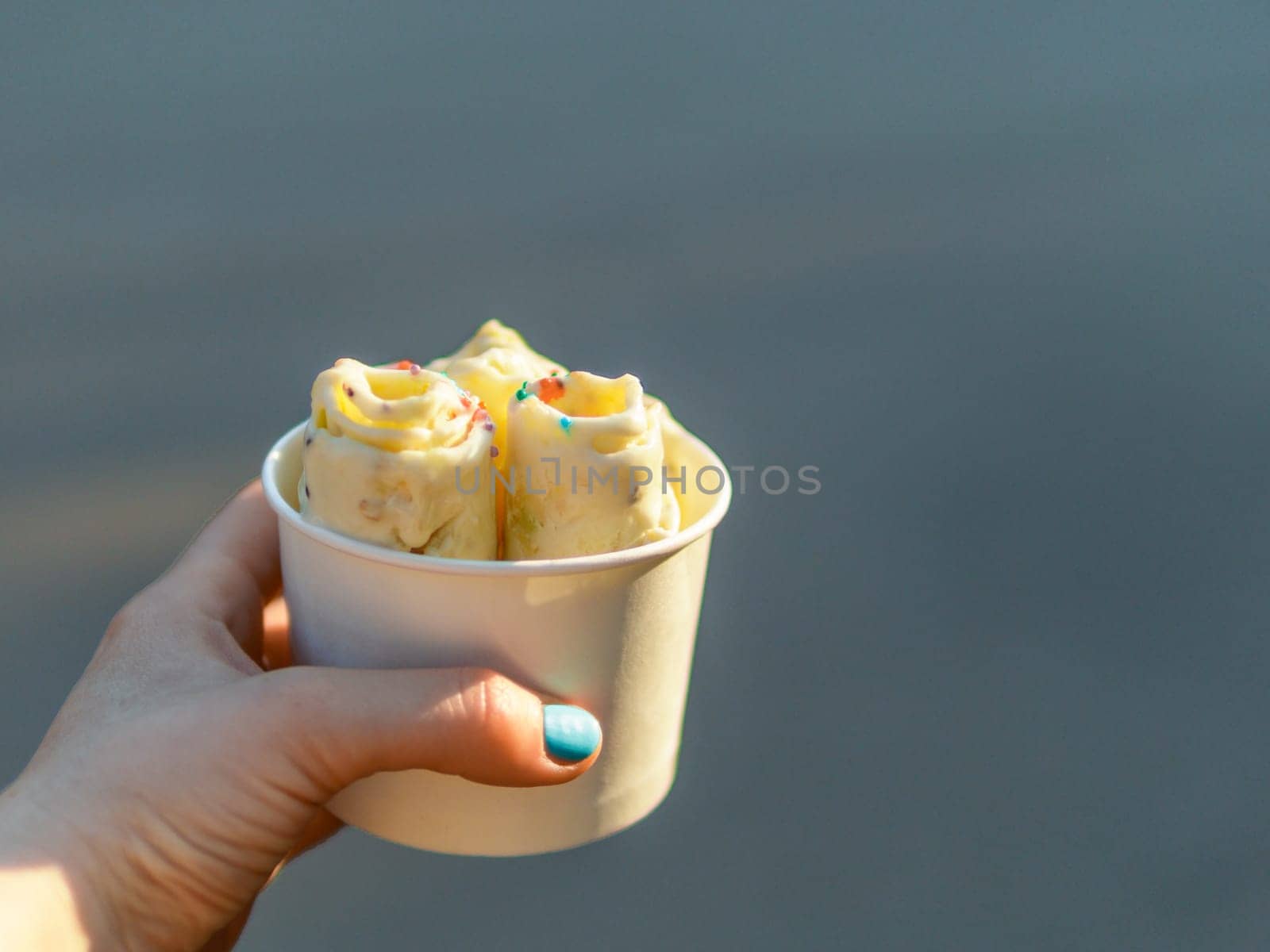 Rolled ice cream in cone cup in woman hand. Woman holds cone cup with thai style kiwi banana rolled ice cream. Outdoor. Natural hard daylight. Copy space right.