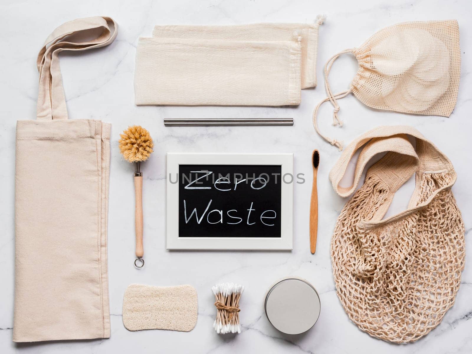 Zero waste concept. Textile eco bags, metal straws, eco-friendly kitchen tools, bamboo toothbrush and cotton buds, reusable cotton pads on white marble background. Top view or flat lay