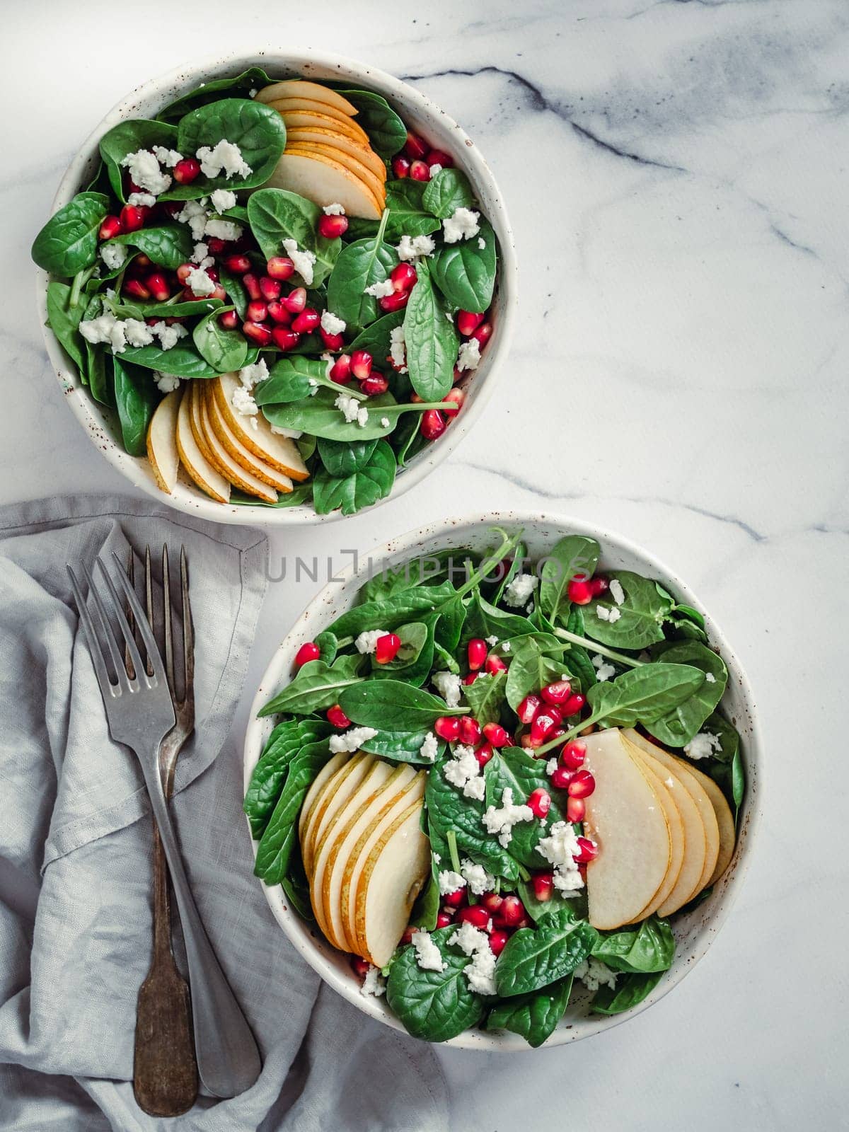 Vegan salad bowl with spinach, pear, pomegranate, cheese on marble tabletop. Vegan breakfast, vegetarian food, diet concept. Vertical. Top view or flat lay.