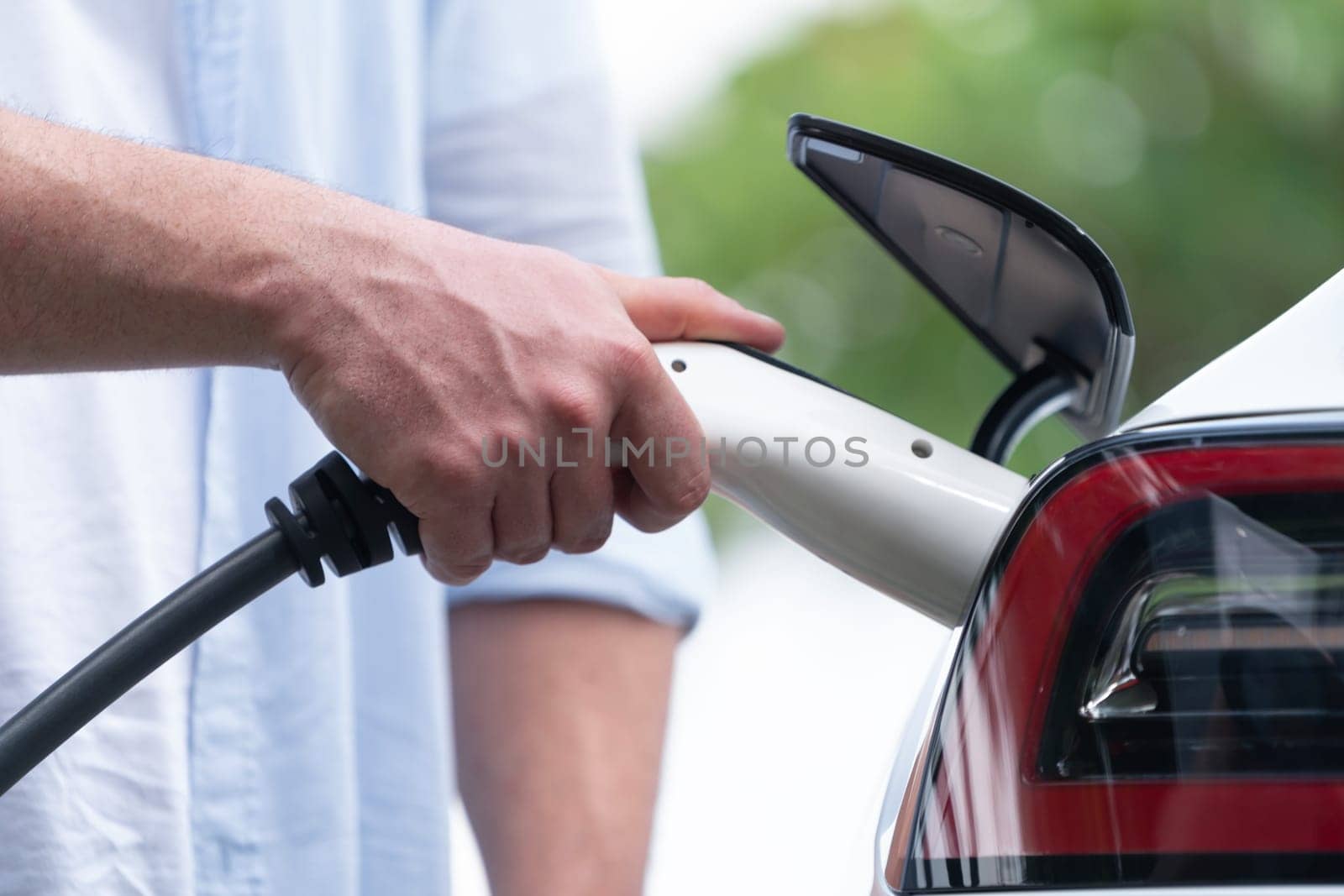 Closeup hand insert and EV charger to recharge EV car's battery from charging station. Alternative energy utilized for transportation with environmental friendly for future sustainability. Synchronos