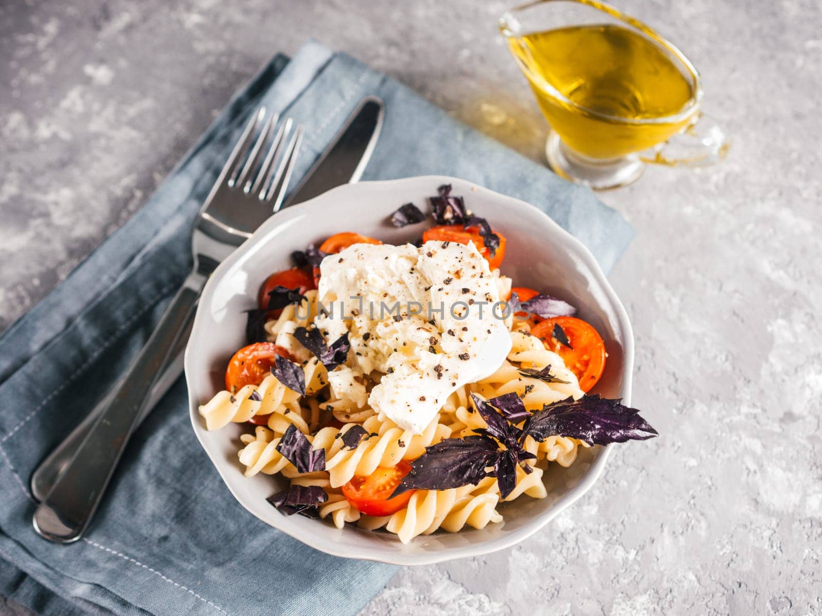 Tasty italian fusilli pasta with cherry, mozarella or buratta cheese and fresh basil. Dish with pasta on gray concrete background. Copy space. Healthy food concept and recipe idea.