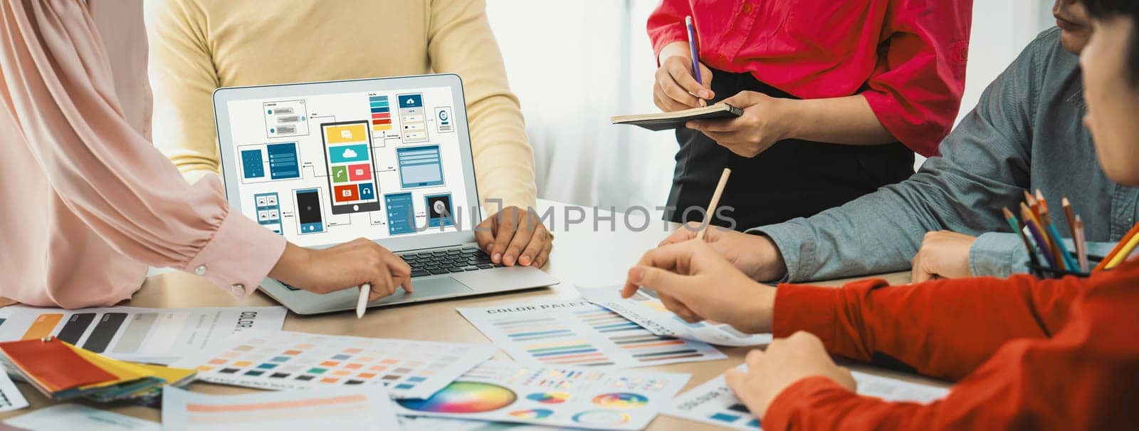 Cropped image of interior designer team presents color by using color swatches while laptop displayed UI and UX designs for mobiles app and website. Creative design and business concept. Variegated.