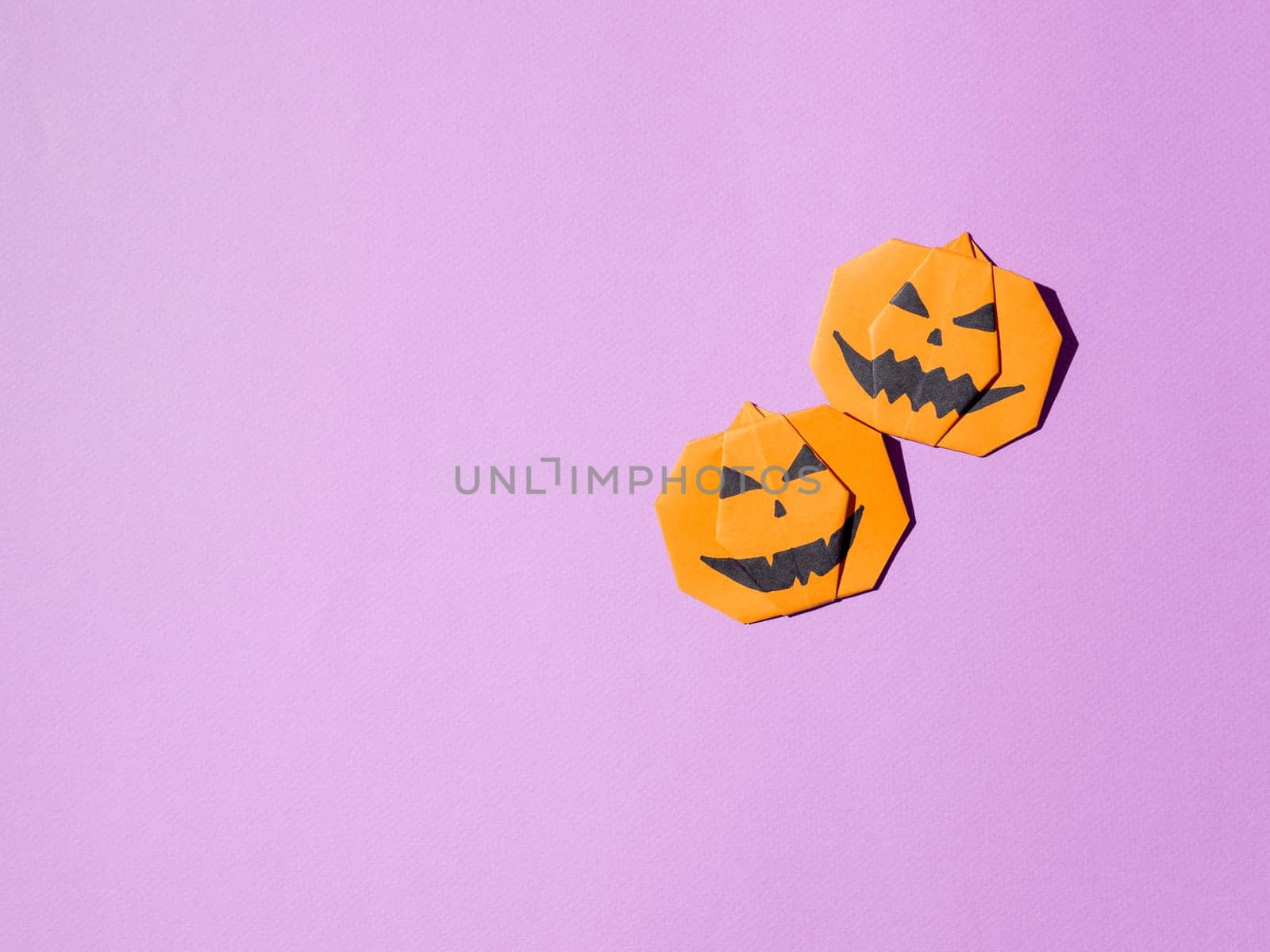 Halloween concept. Paper origami pumpkin on bright purple background. Simple idea for halloween - easy made paper pumpkins on trendy Crocus Petal lilac color background. Copy space for text.