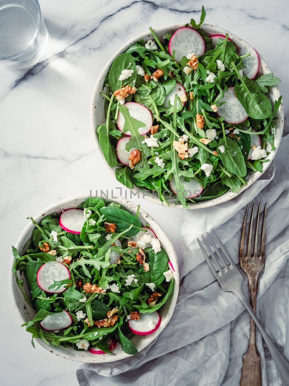 Vegan salad bowl with arugula, spinach, radish, coconut crumble or cottage cheese,walnut.Top view.Vegan breakfast, vegetarian food, diet concept. Two bowls with salad on white marble tabletop.Vertical